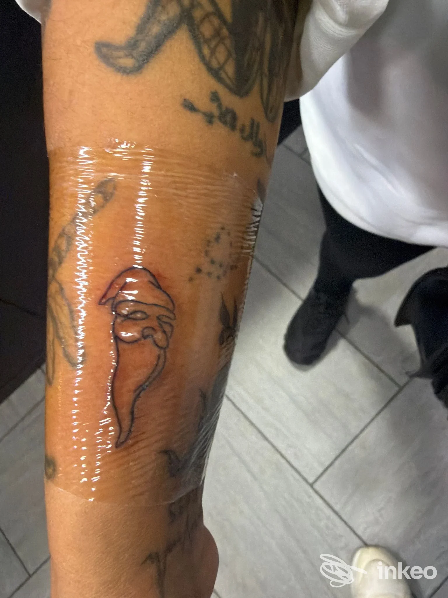 Braccio di una persona con tatuaggio disegnato a spina di pesce, coperto da pellicola trasparente; si intravede parte del corpo e dei vestiti, Napoli, studio Naples Tattoo Souvenir.