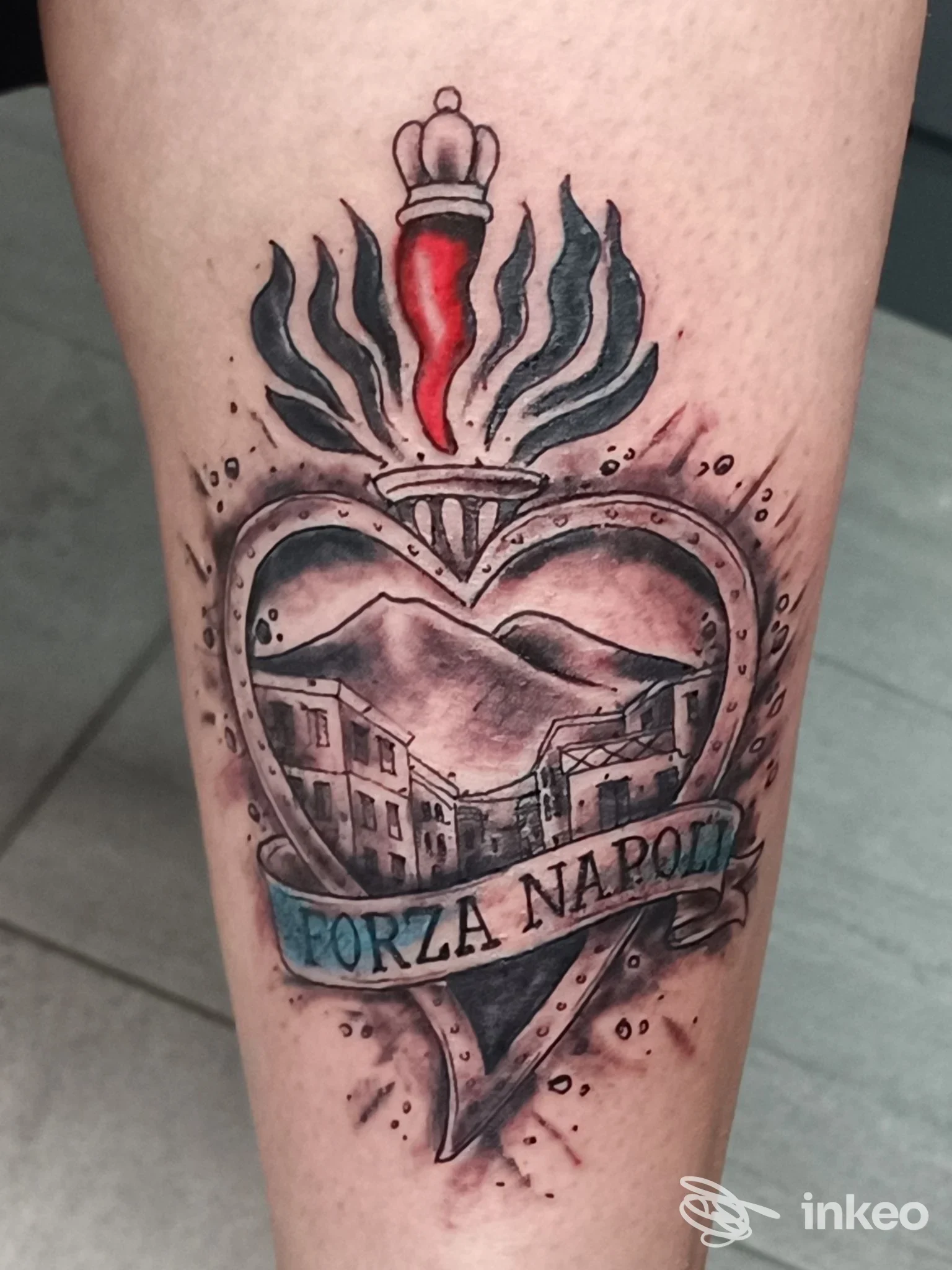 Tattoo realistico su pelle: cuore decorato da una corona, scena di Napoli all’interno del cuore e nastro con Forza Napoli, eseguito su pelle.