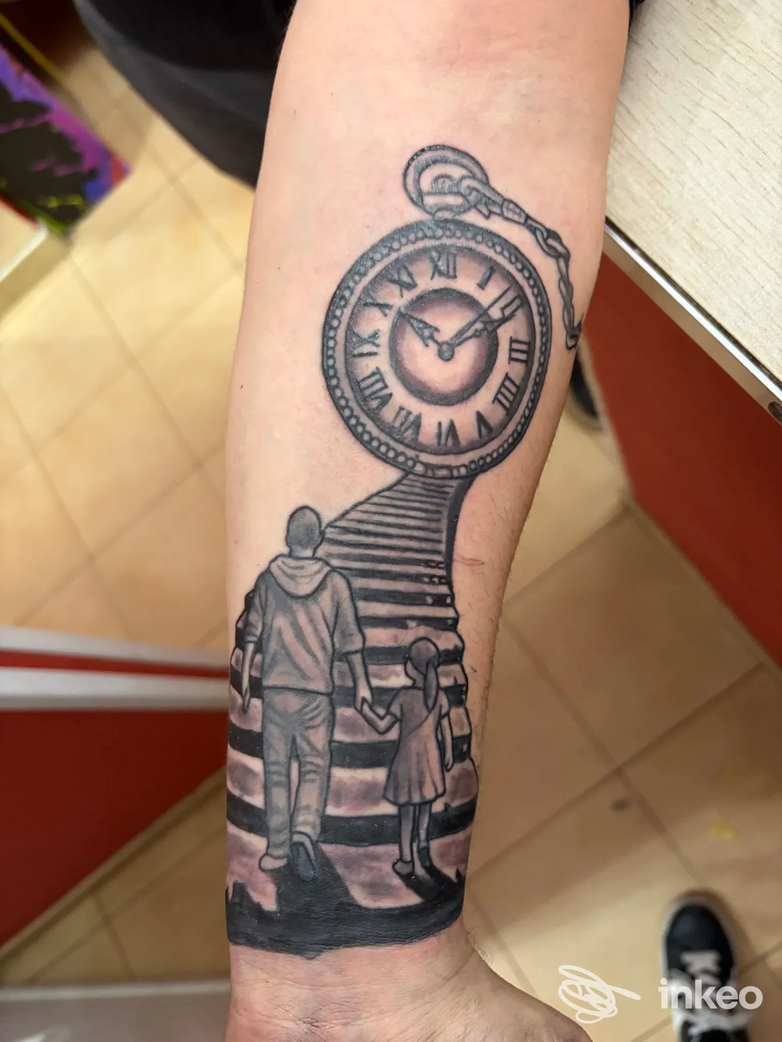 Braccio raffigurante un orologio da tasca inciso con figure in silhouette e gradient di ombre, tatuaggio realizzato sulla pelle