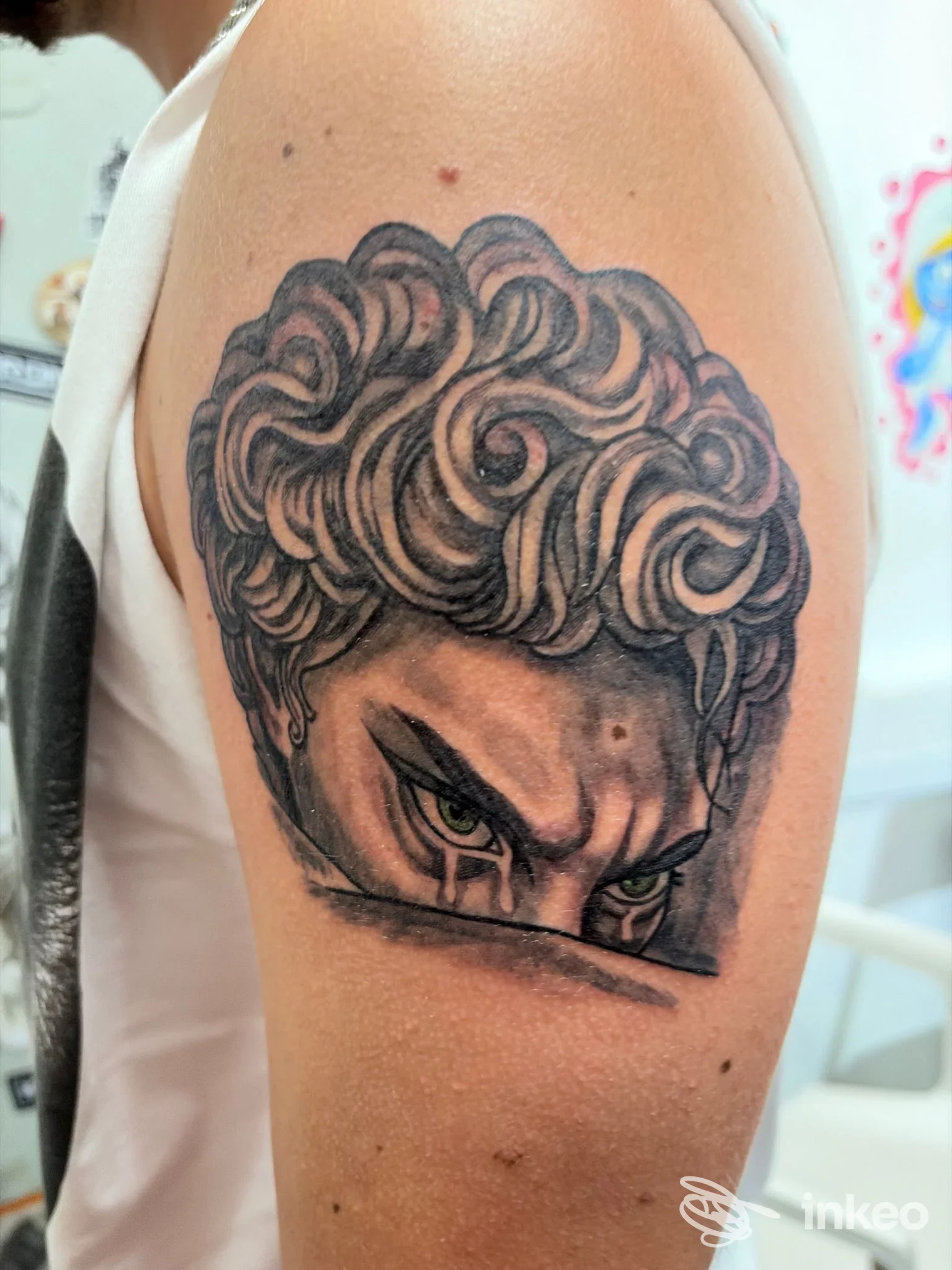 Tatuaggio realistico sul braccio sinistro, ritratto stilizzato di occhi intensi e capelli ricci, con linee scure e sfumature, realizzato su pelle, presso Karont Tattoo, Atripalda.