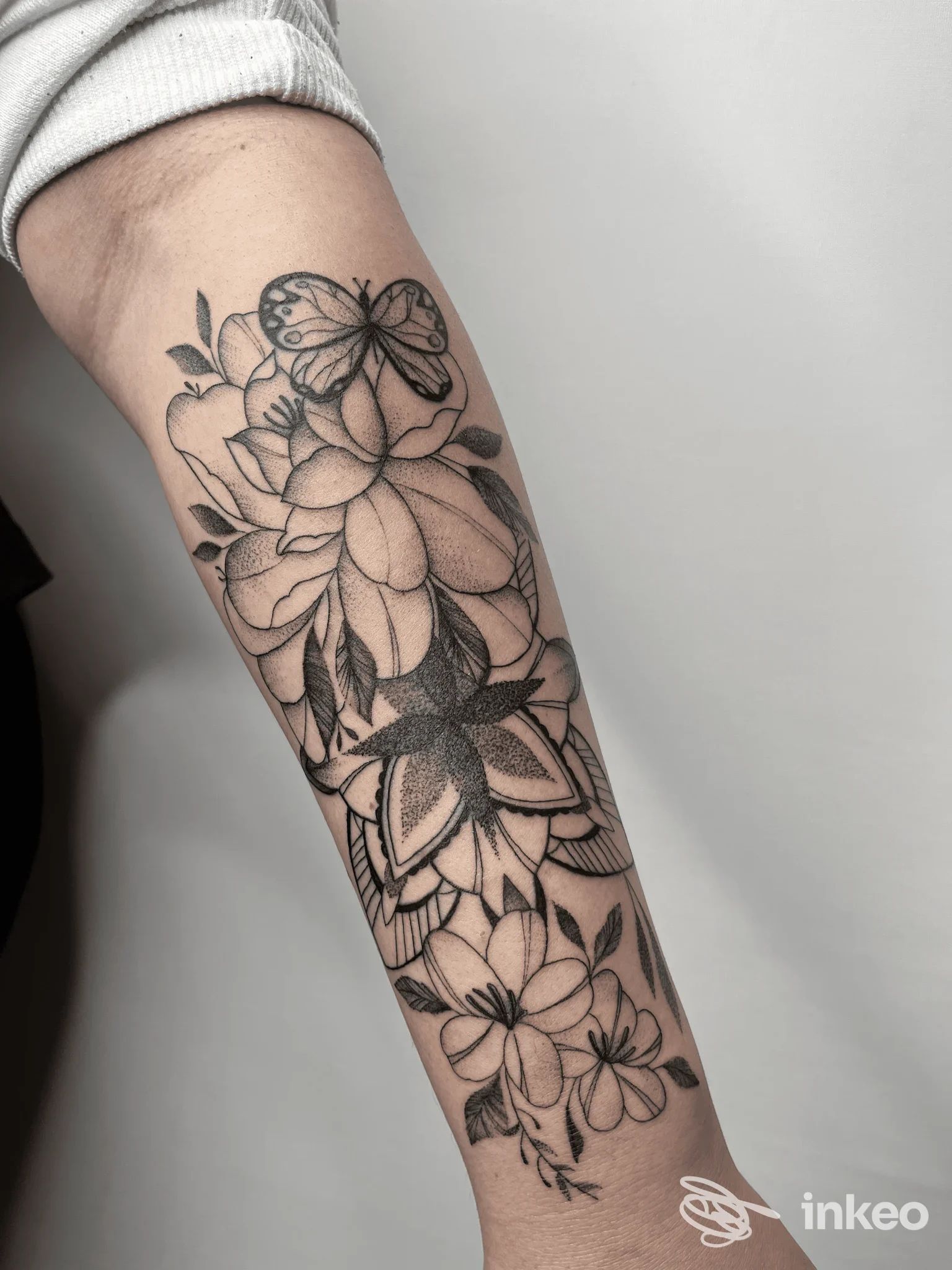 Tattoo a fiori e farfalle su avambraccio, in stile linework, inchiostrato in nero su pelle chiara, mostrato a braccio piegato senza viso.