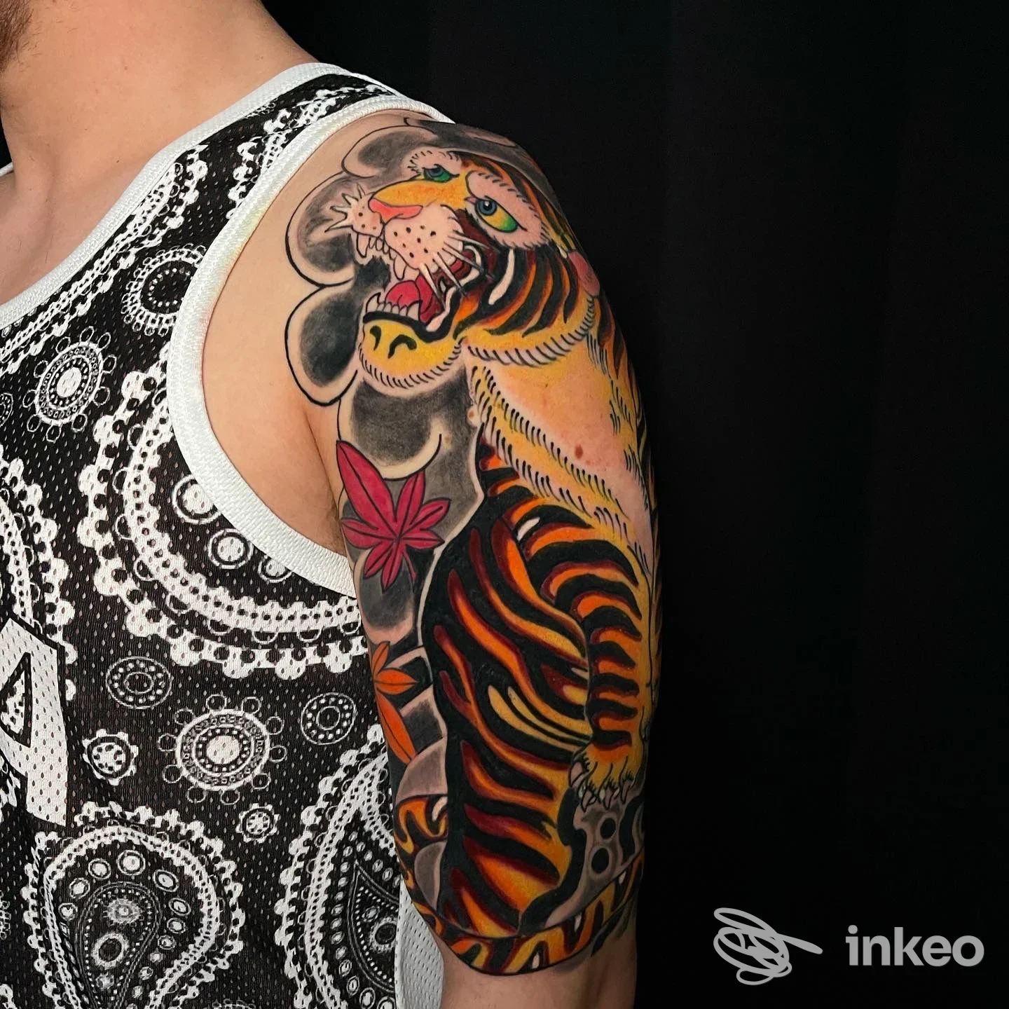 Braccio di una persona con tatuaggio colorato a strisce di tigre, oltre ad altri elementi, ben visibile sulla pelle contro sfondo scuro.