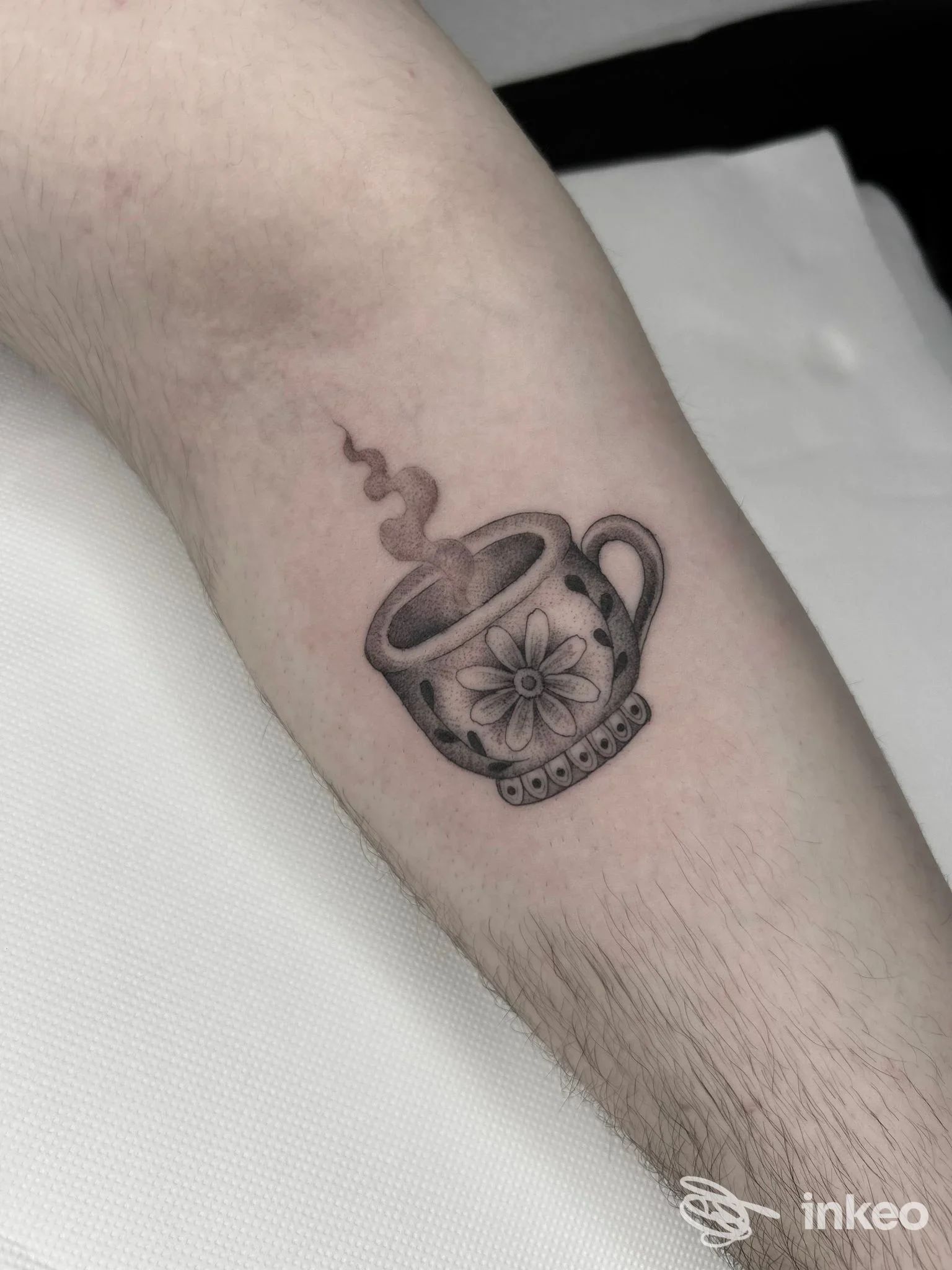 Tattoo visibile sull'avambraccio raffigurante una tazza fumante decorata con fiore, eseguita direttamente sulla pelle.