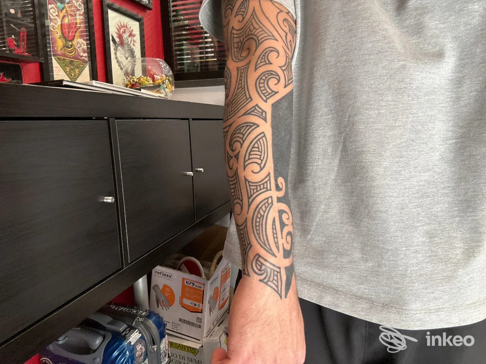 Braccio di una persona con tatuaggio a maniche lunghe visibile sul braccio sinistro, motivo geometrico/tribale ben definito sulla pelle, lo sfondo mostra lo studio Little Star Tattoo a Napoli.