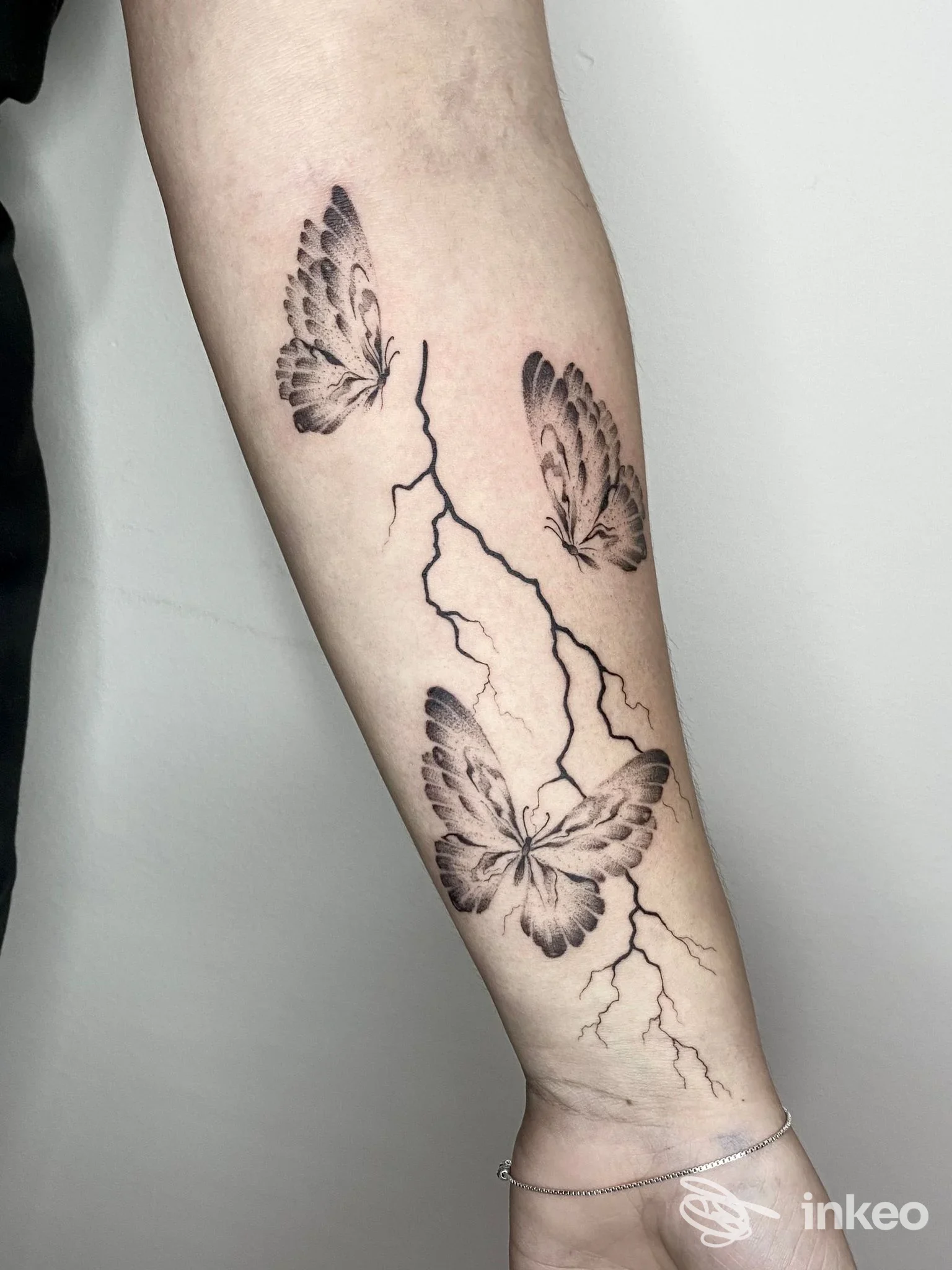 Avambraccio con tatuaggio di tre farfalle nere attorno a una linea di crepa/fulmine; tatuaggio ben definito su pelle.