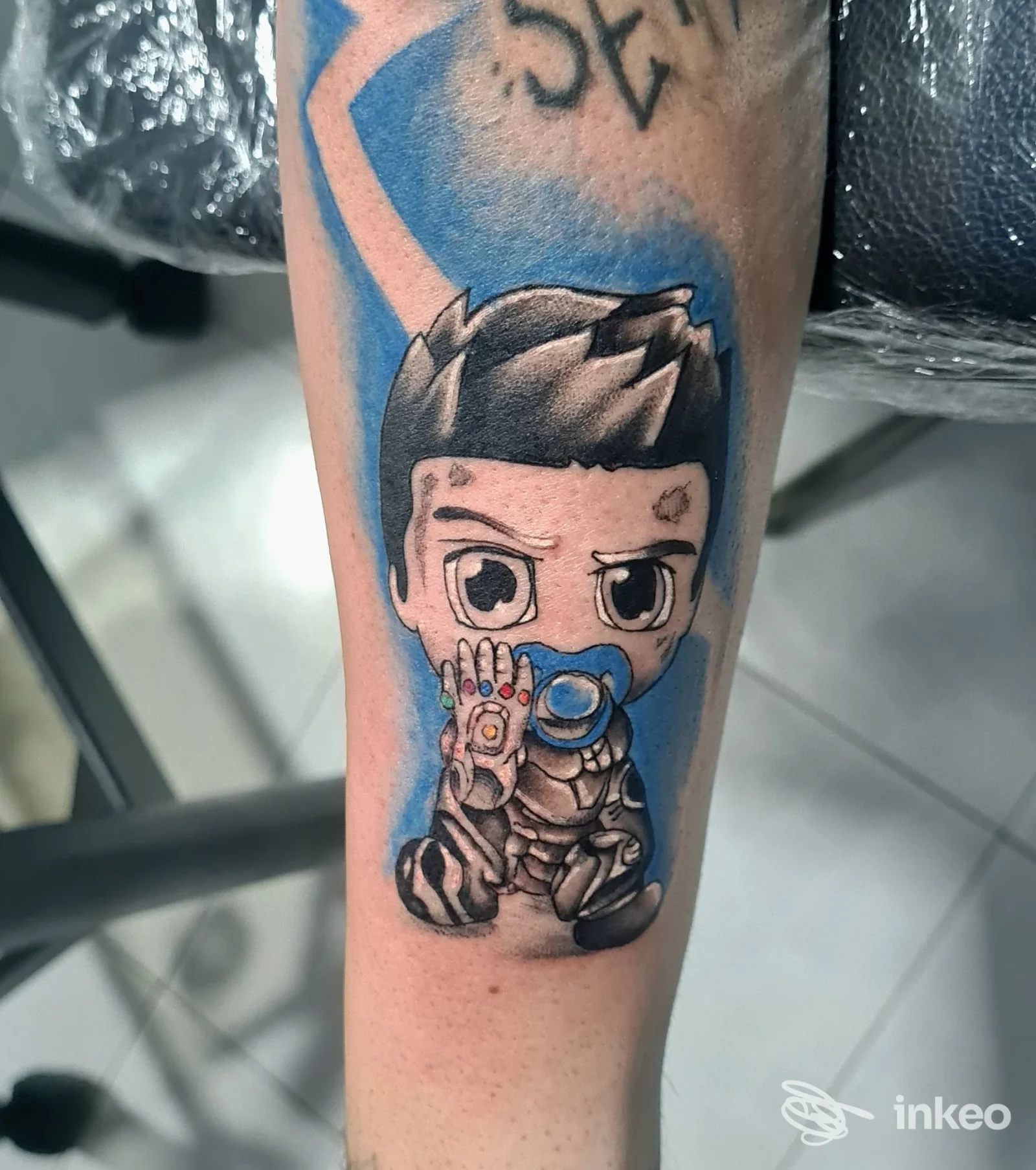 Tatuaggio sul braccio raffigurante un personaggio cartoonesco con occhi grandi, capelli scuri e guanto blu, su sfondo azzurro.