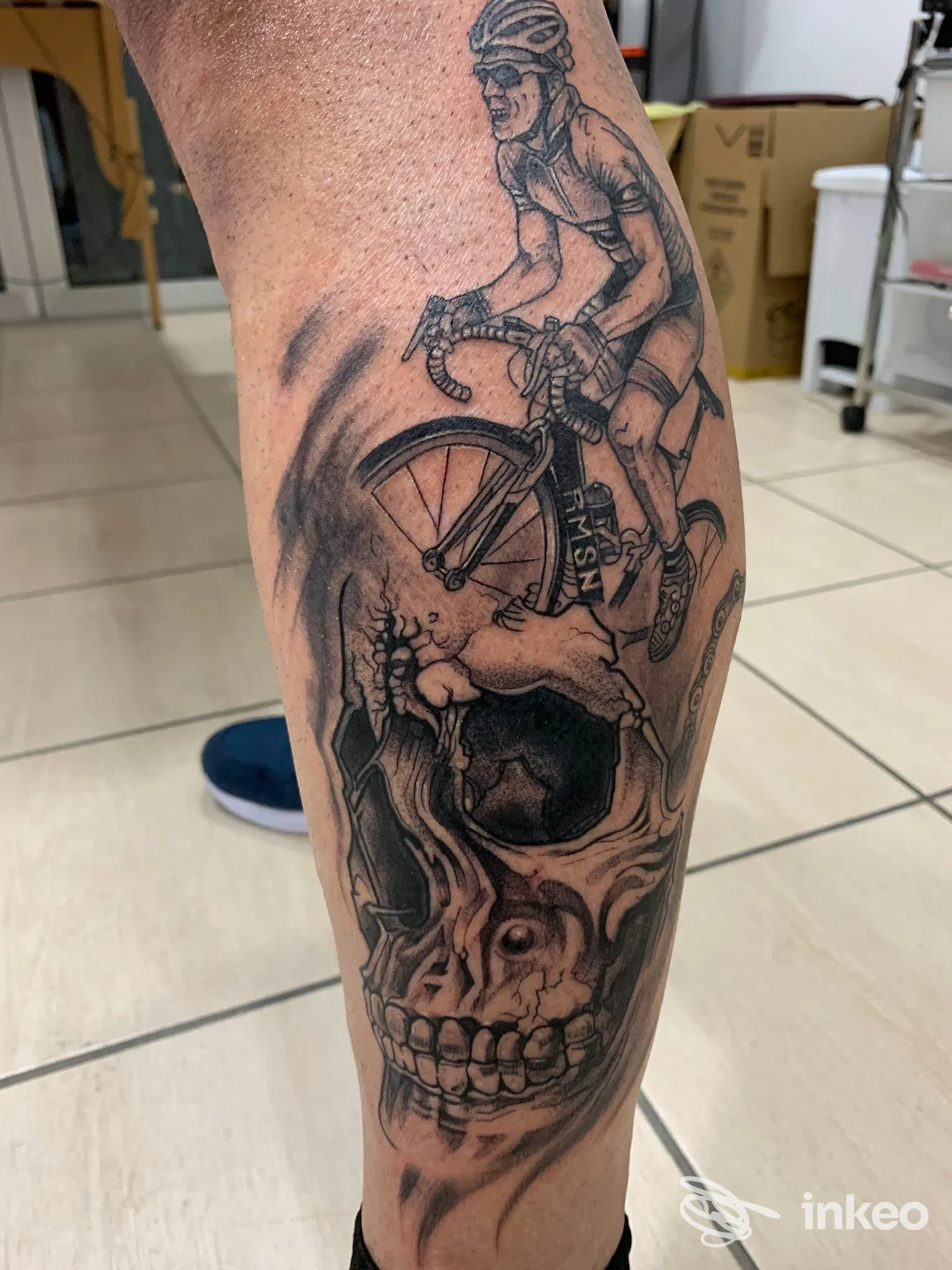 Tatuaggio sul polpaccio raffigurante una testa di teschio e una bicicletta, realizzato da REZ STUDIO TATTOO a dei rossi, schiarito in bianco e nero.