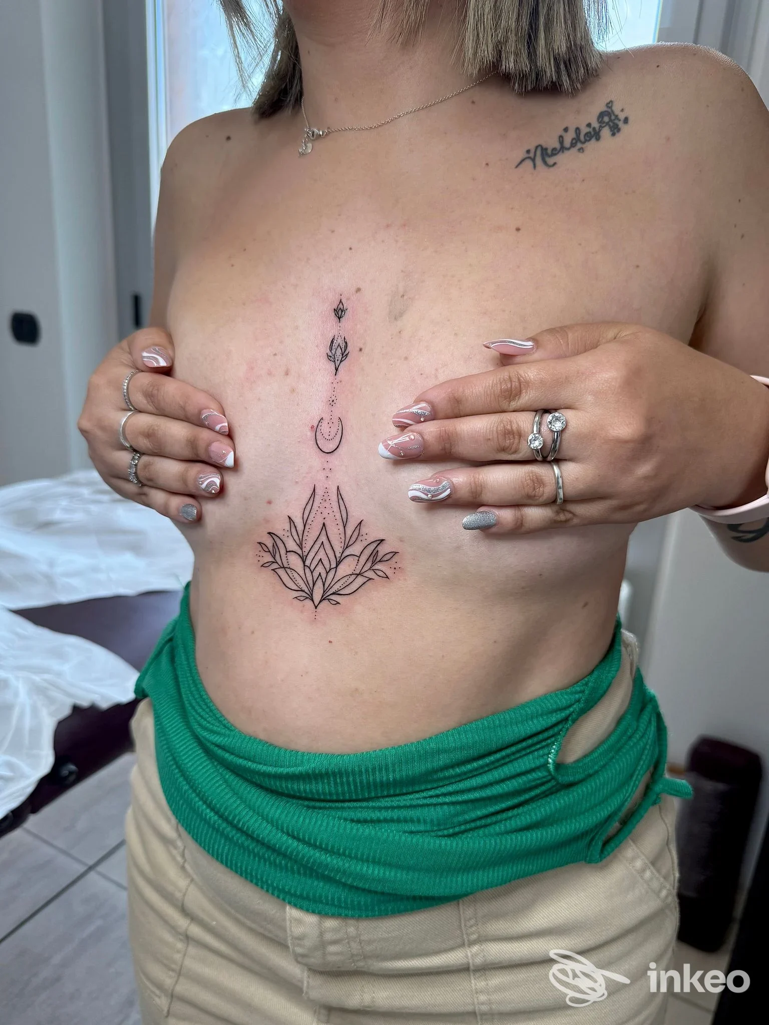 Donna mostra una serie di tatuaggi sul torace: disegno centrale a forma di fiore con elementi verticali, eseguiti sulla pelle, nessun overlay sociale visibile.