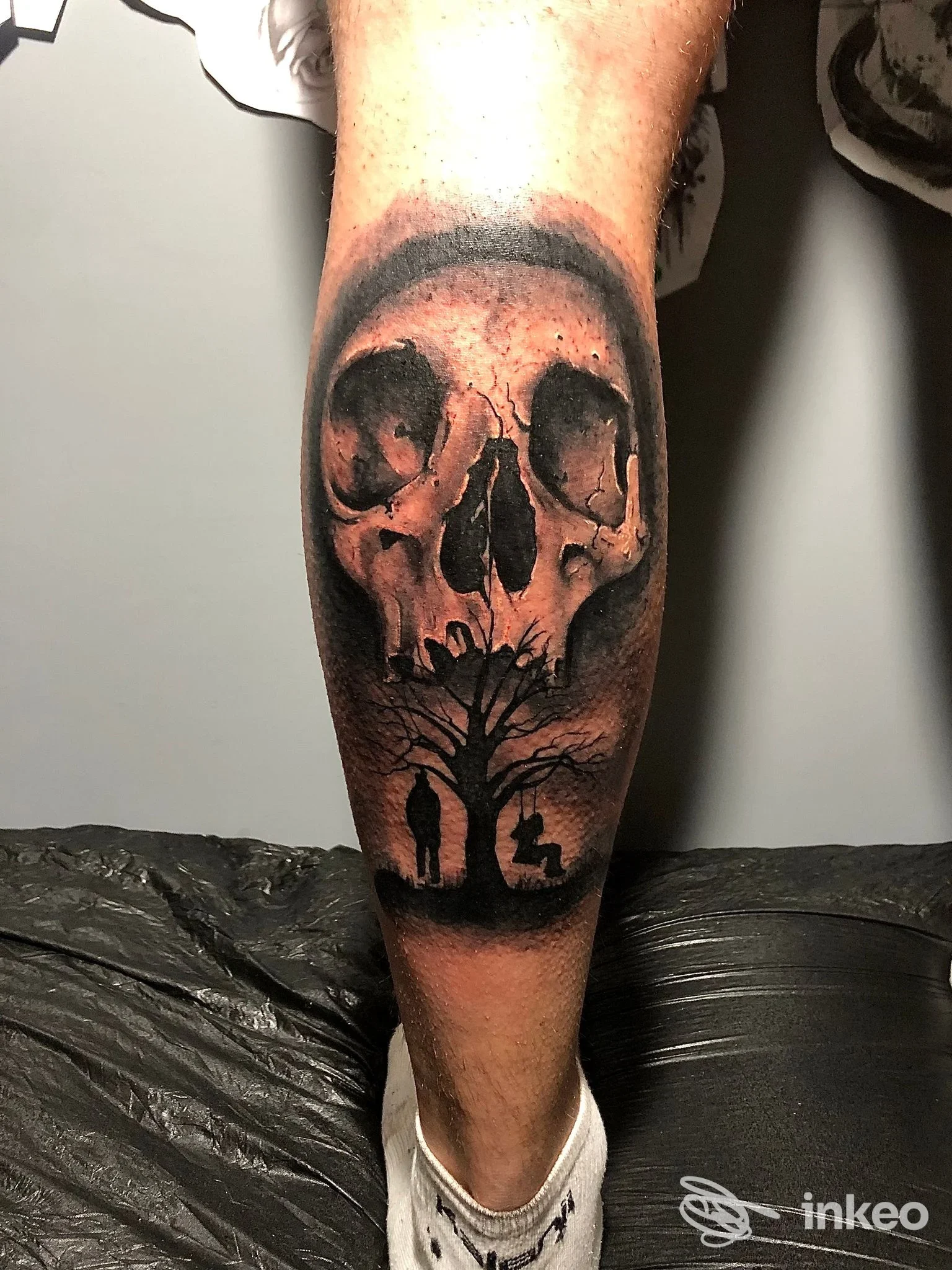 Tatuaggio realistico sul polpaccio raffigurante un teschio con albero e silhouettes, eseguito sulla pelle; stile dark con ombre marcate, studio The Black Deer, Atripalda.
