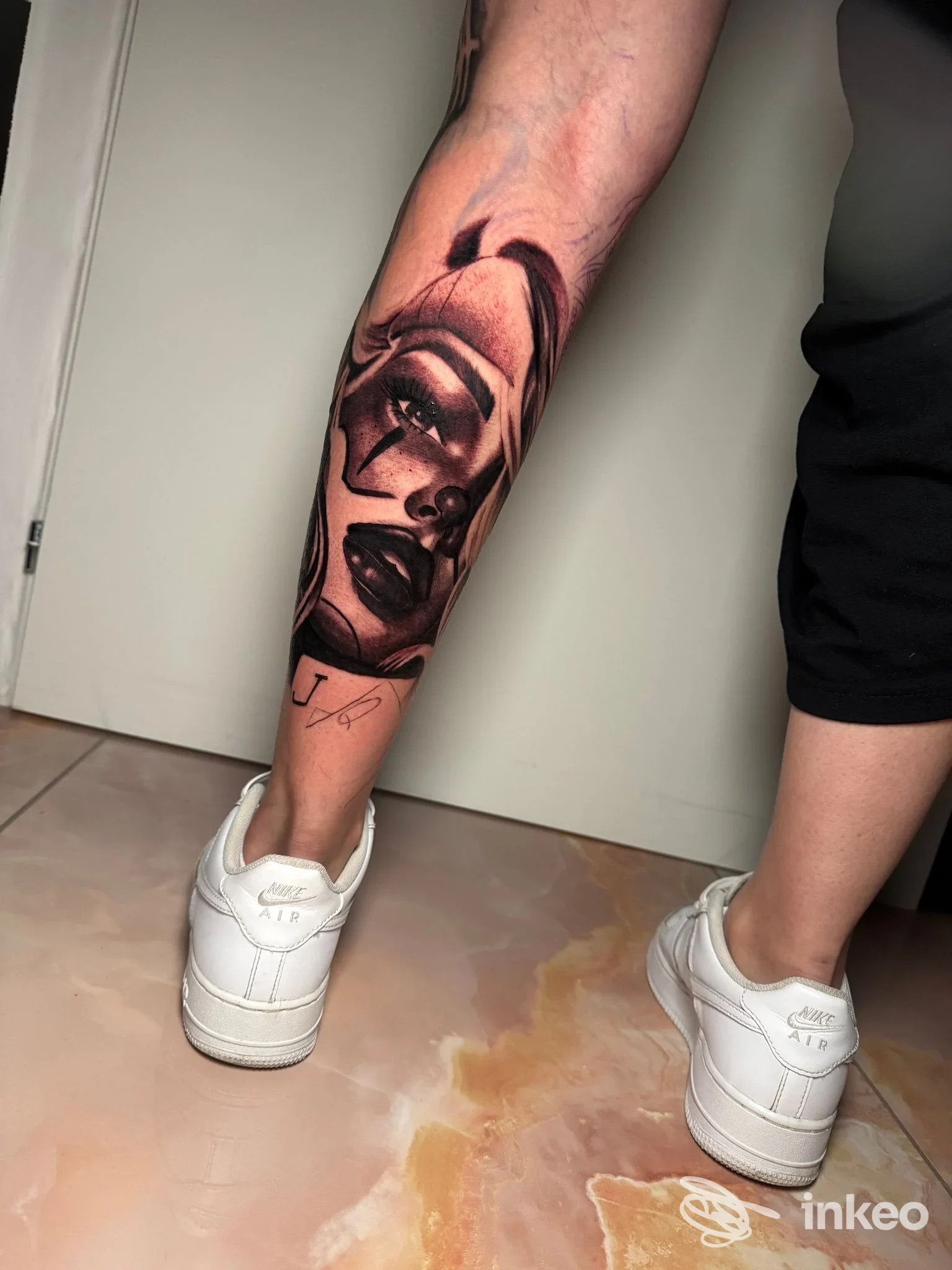 Tattoo realistico su gamba raffigurante una donna con trucco marcato, realizzata sulla pelle; si vede solo una porzione della gamba con la sneakers bianche, nessun overlay o immagine di schermo.