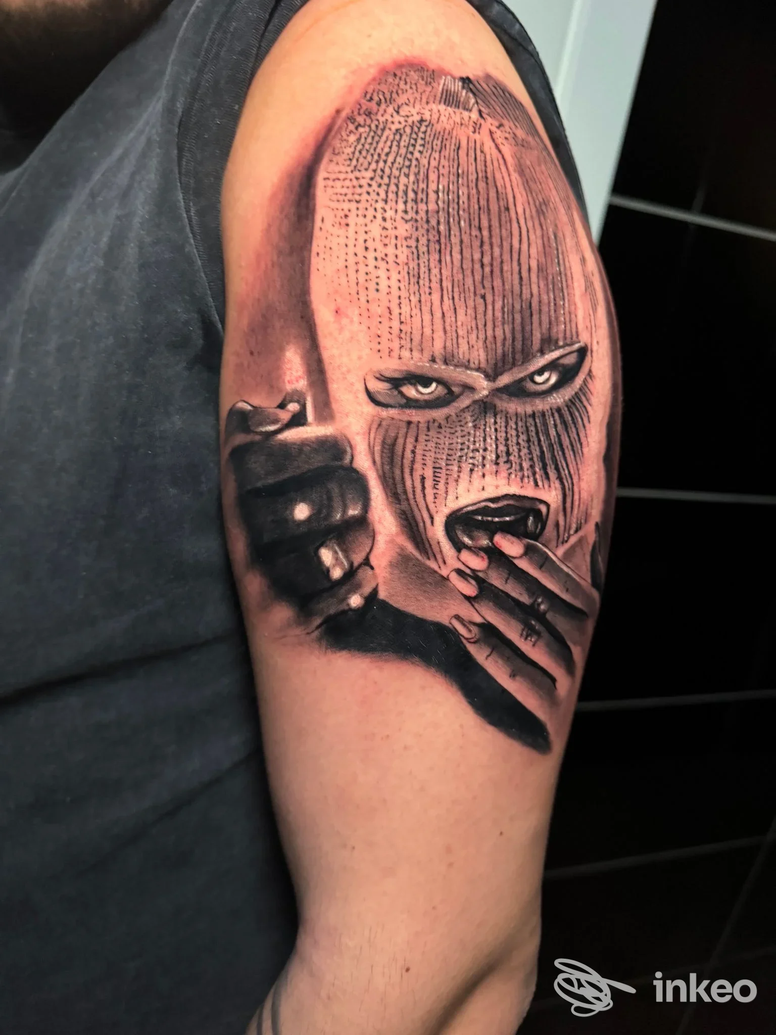 Tattoo sul braccio realizzato da Orion Ink a Qualiano: figura incappucciata che punta e si porta le dita alla bocca, in tonalità nero-grigio.