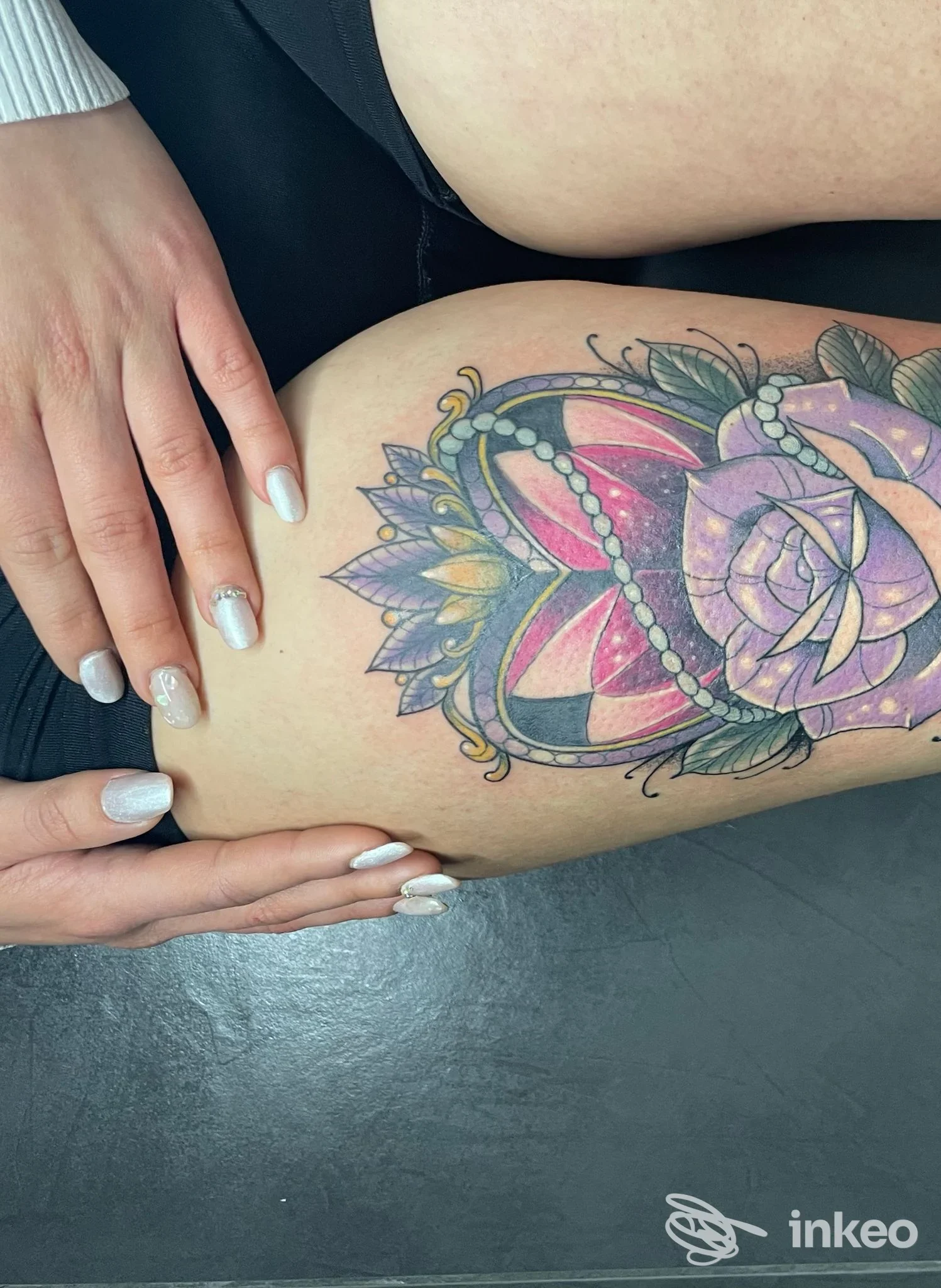 Tattoo colorato a mandala su gamba, eseguendo sul tessuto della pelle; firma visibile sul fianco sinistro, con mani della modella che toccano la zona tatuata.