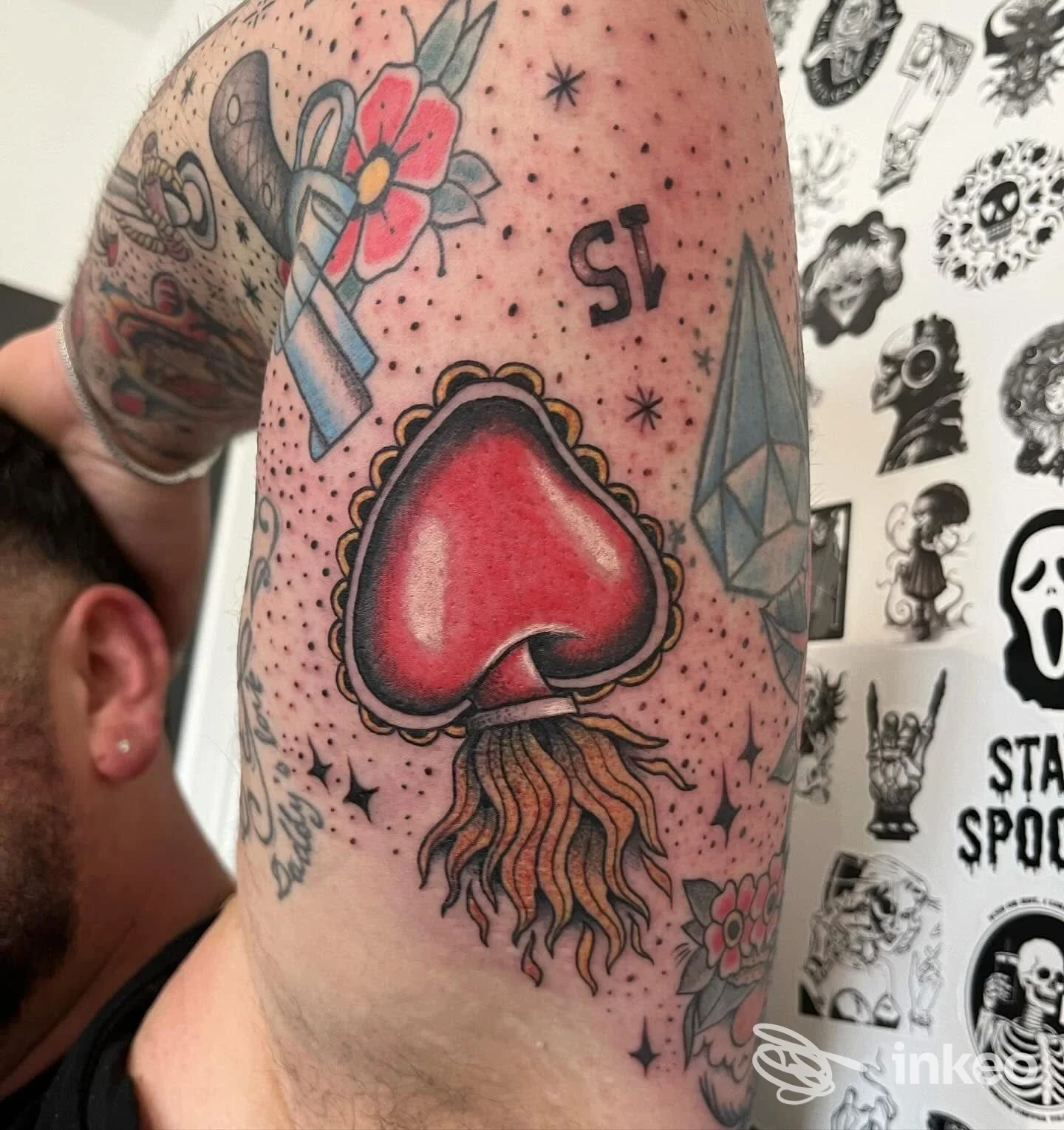 Tattoo su braccio superiore: cuore rosso con contorno scuro e decoro a viti e onde, accompagnato da altre grafiche sullo sfondo.