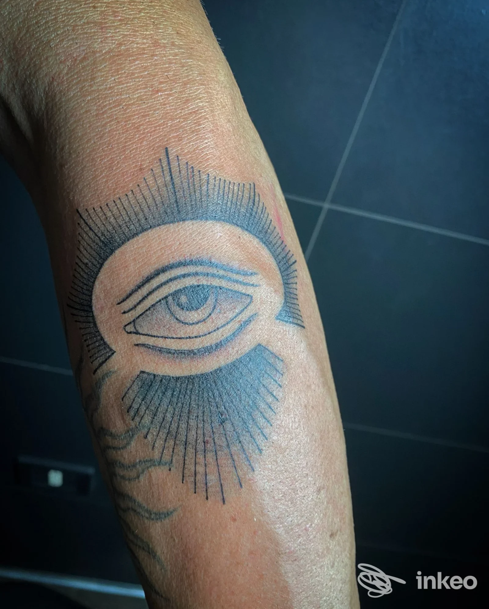 Braccio con tatuaggio: un occhio stilizzato con dettagli lineari scuri, realizzato sulla pelle; tono di pelle nitido e contour ben definito.