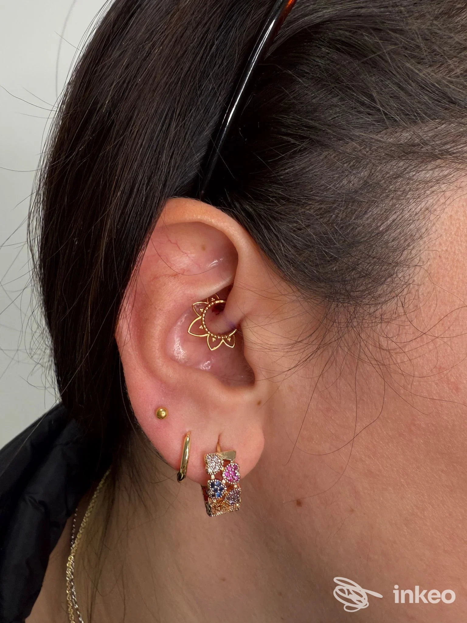 Orecchio sinistro con più piercing: cerchi dorati, barra verticale e orecchino con componente incastonato. foto in studio Danierix Piercing Studio, Napoli.
