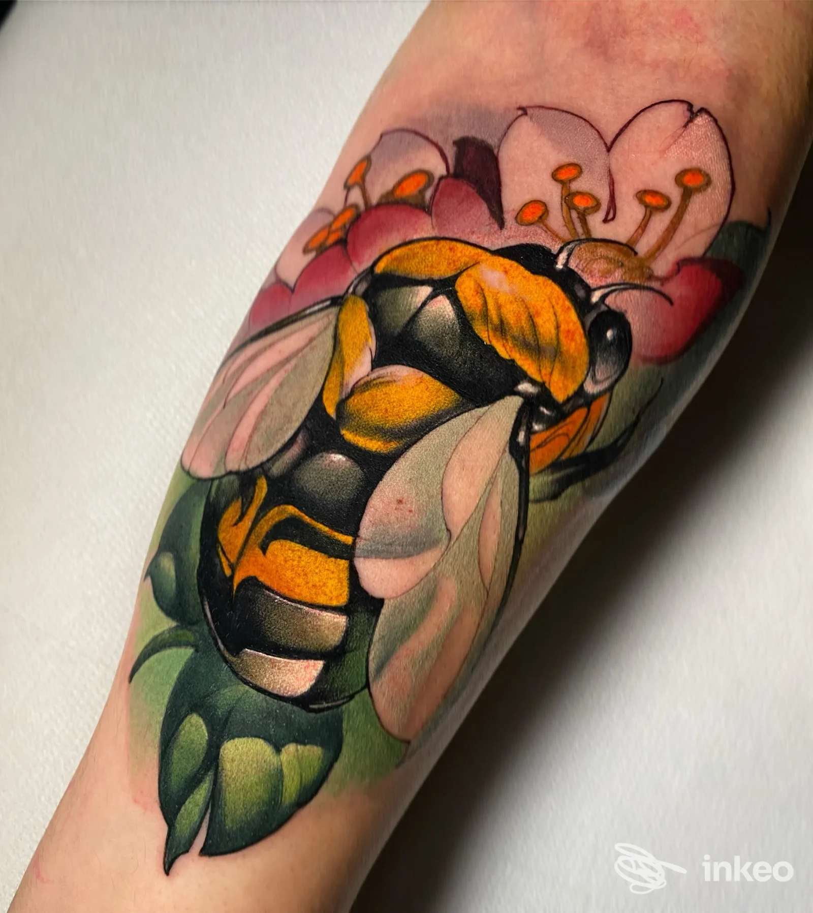 Tatuaggio colorato su braccio raffigurante un'ape gialla e nera tra fiori rosa e foglie verdi, realizzato direttamente sulla pelle.