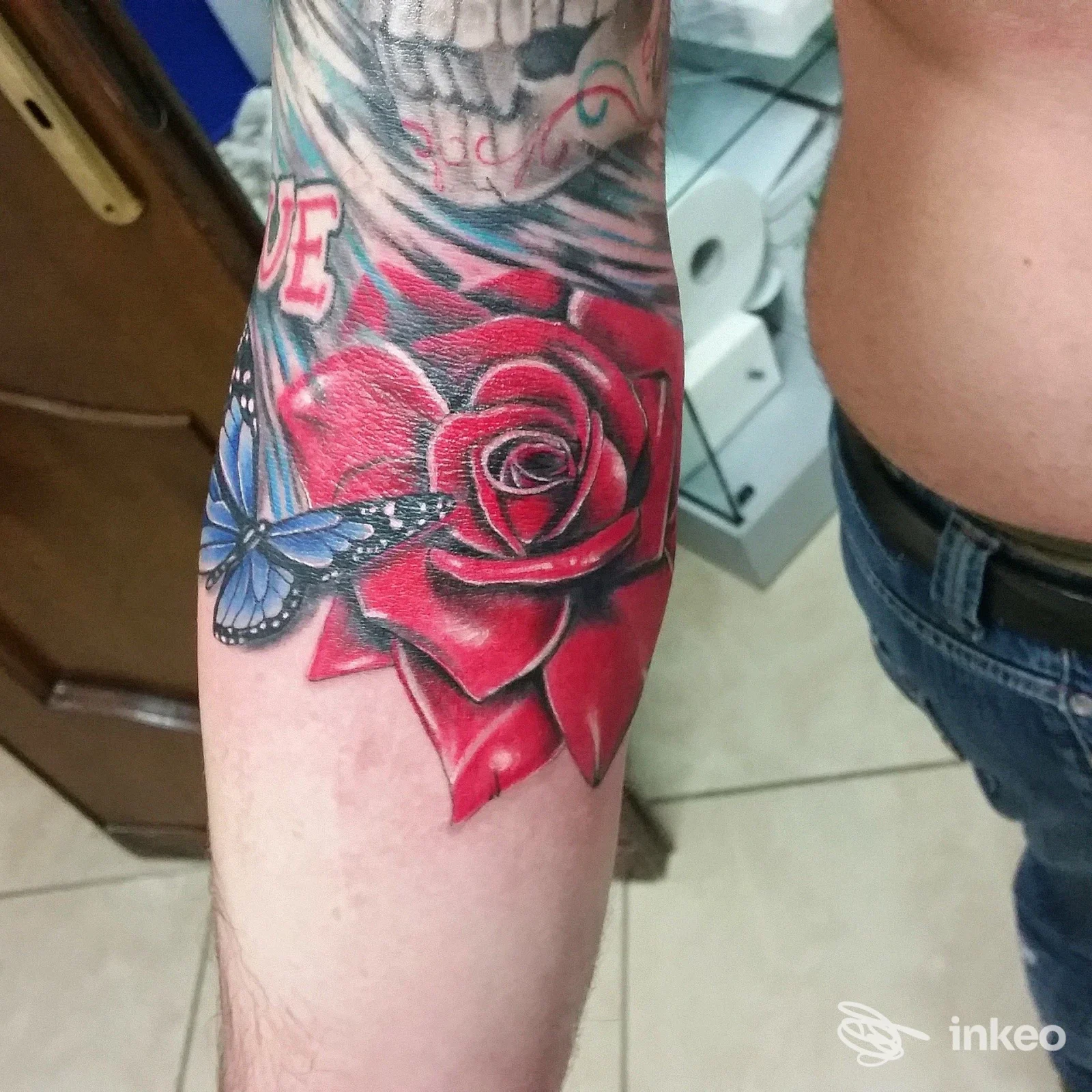 Tattoo completo su avambraccio raffigurante una rosa rossa con sfondo e farfalla blu, eseguito su pelle reale, studio Napoli, Studio14 Tattoo Piercing.