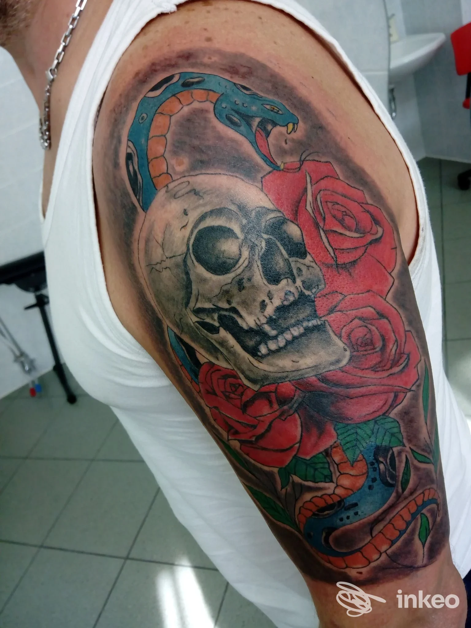 Tatuaggio realizzato sulla parte superiore del braccio: teschio, serpente e rose colorate con sfondo scuro, realizzato su pelle, senza viso visibile. Studio Lady Blue Diamond, Ariano Irpino.