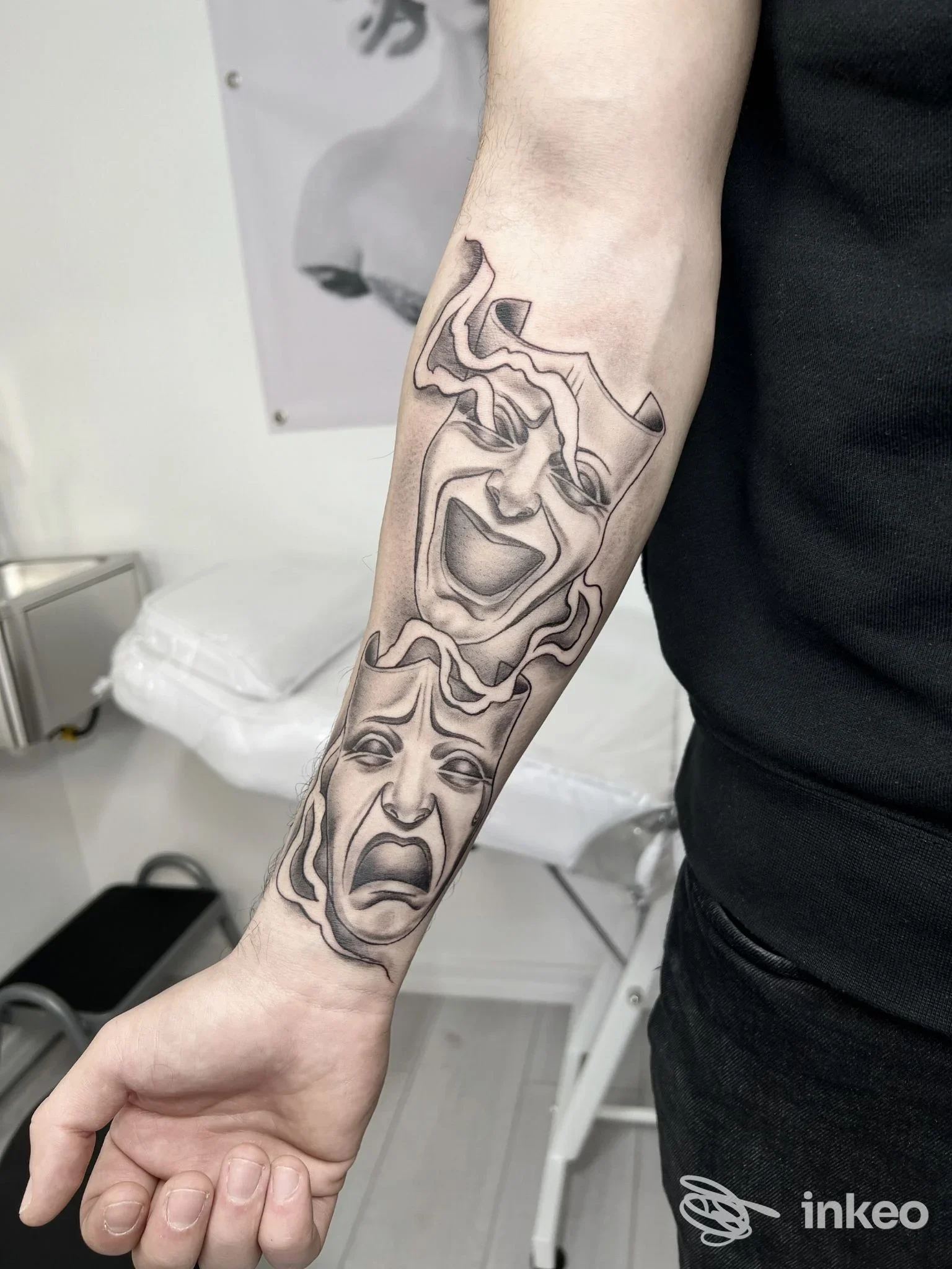 Tatuaggio su avambraccio raffigurante maschere teatrali comedy e tragedy, eseguito direttamente sulla pelle con linee nere nette.