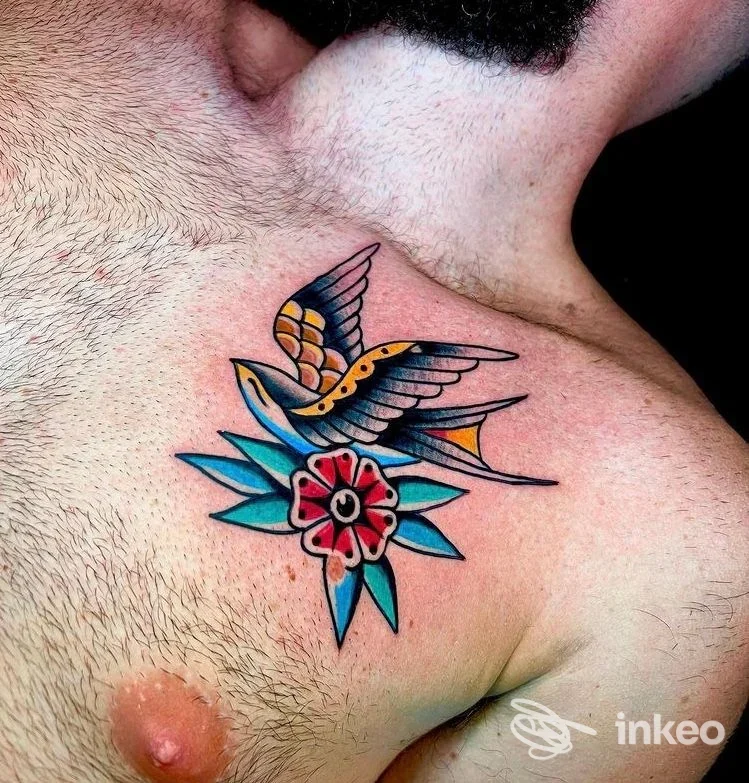 Tatuaggio colorato di un colibrì in volo con fiore su una spalla, stile tradizionale/neo-tradizionale, colori vividi e linee nette.