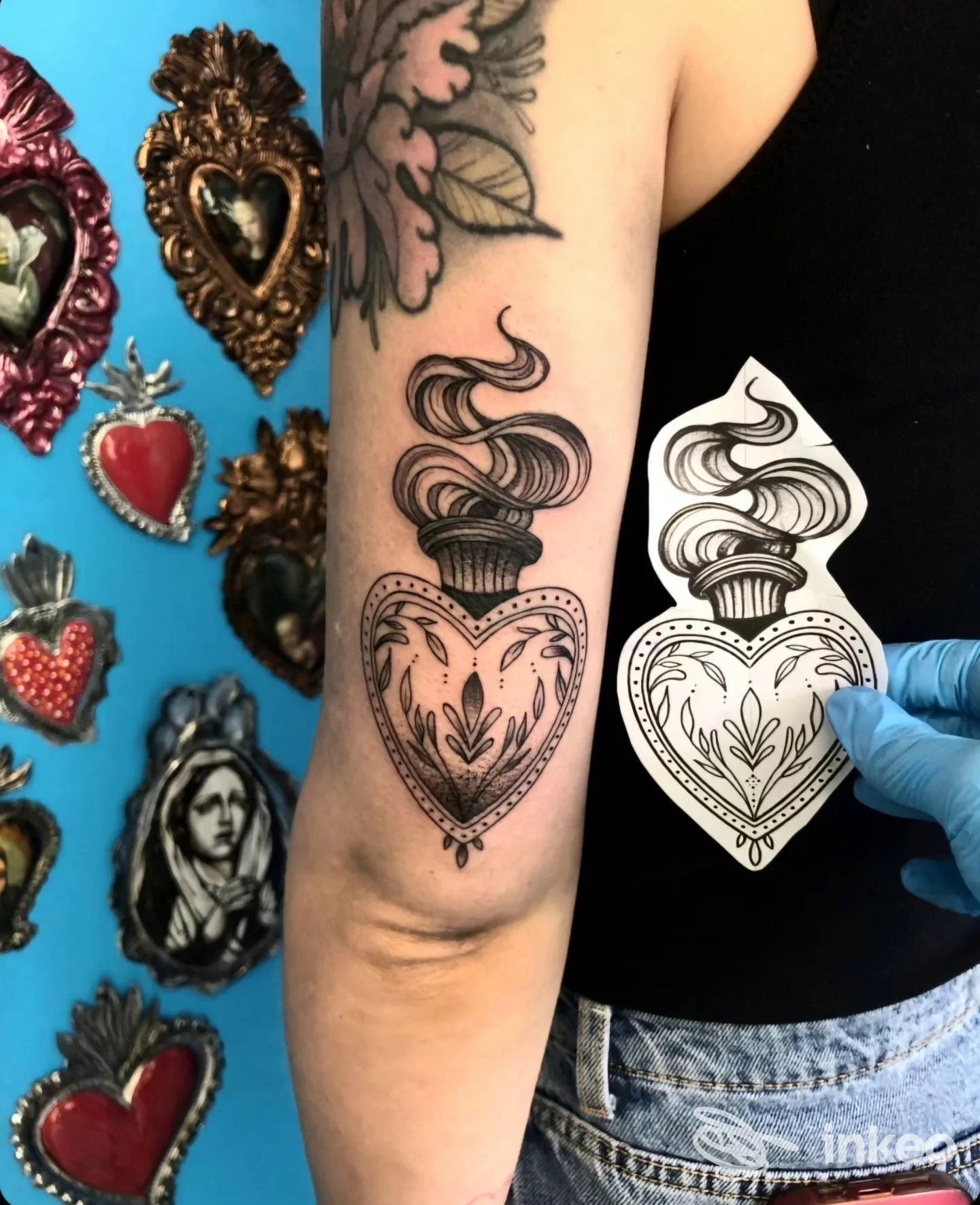 Tatuaggio sull'avambraccio di cuore decorato con ornamenti e fumo, confrontato con una bozza stencil su foglio bianco, nello studio Tattoo Claire.