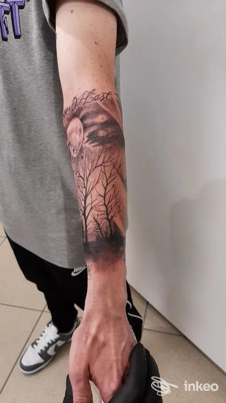 Avant-braccio mostra un tatuaggio realistico a tema paesaggio notturno: alberi senza foglie e una luna parzialmente visibile; la parte visibile è il braccio sinistro, con ombre e linee sottili. Studio Guerra Tattoo a Apice Nuovo.