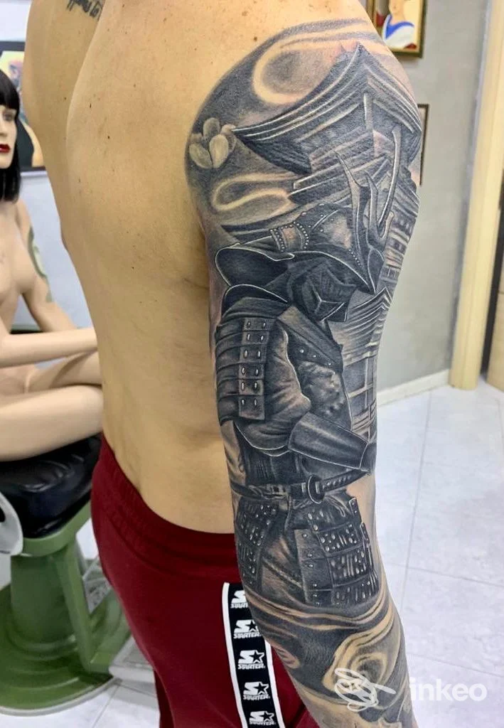 Tatuaggio a manica visibile sul braccio di una persona, in bianco e nero, con dettagli di tessuti e sfumature.