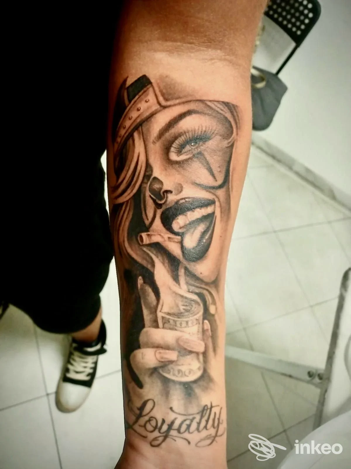 Tatuaggio realistico sull'avambraccio raffigurante una donna con cappello e oggetti, accompagnato dalla scritta Loyalty; studio Modetattoo, Montella.