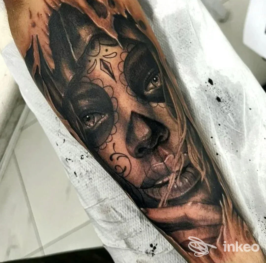 Tattoo realistico su braccio raffigurante una faccia, in bianco e nero con sfumature e dettagli accurati, parte di una composizione più ampia.