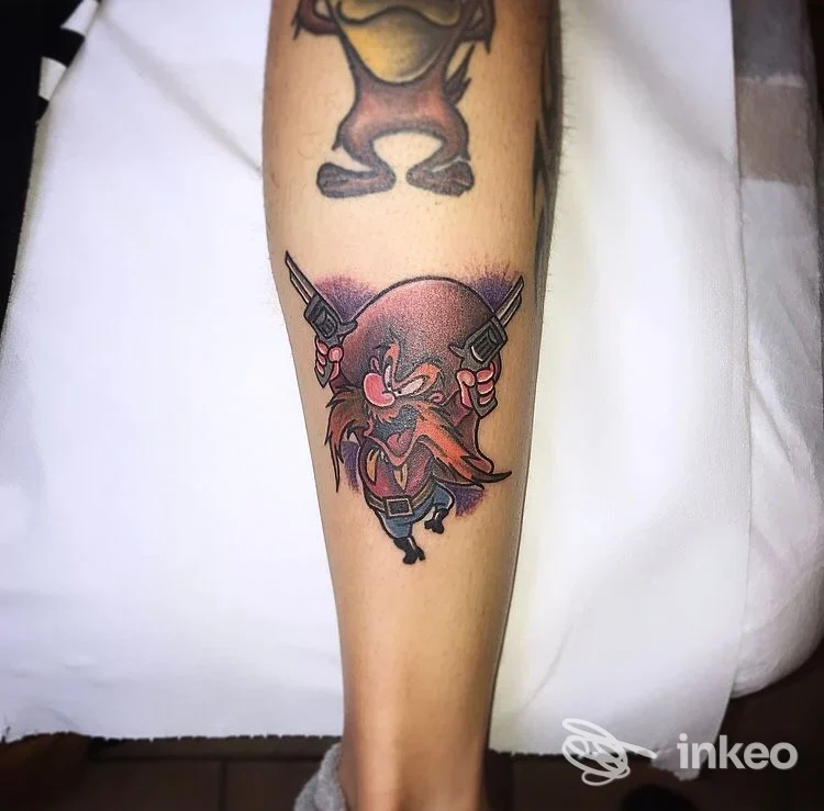 Tatuaggio realistico su avambraccio: personaggio cartone animato con due pistole, colori vividi, contorni neri marcati.