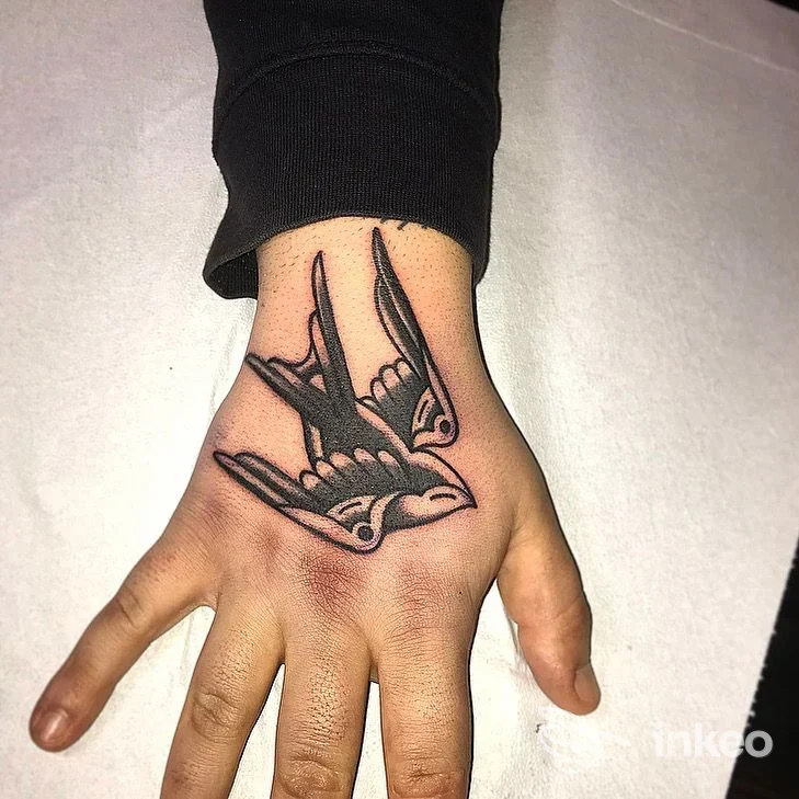 Tattoo su mano destra raffigurante due rondini nere, realizzato sulla pelle in stile linework, senza visibilità di volto né elementi di interfaccia.