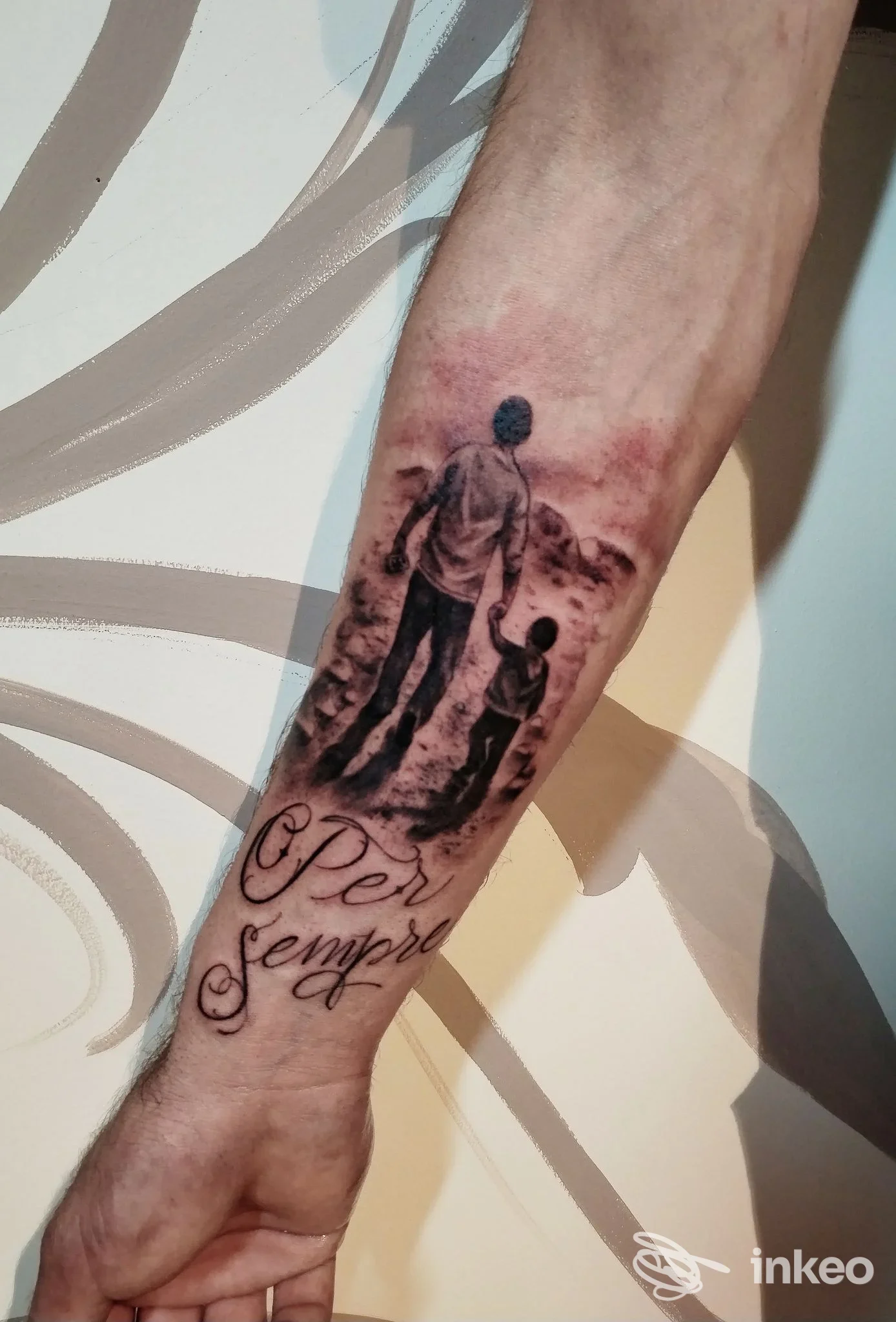 Tattoo sull'avambraccio raffigurante una figura adulta che tiene la mano di un bambino, sfumato sullo sfondo con testo elegante.