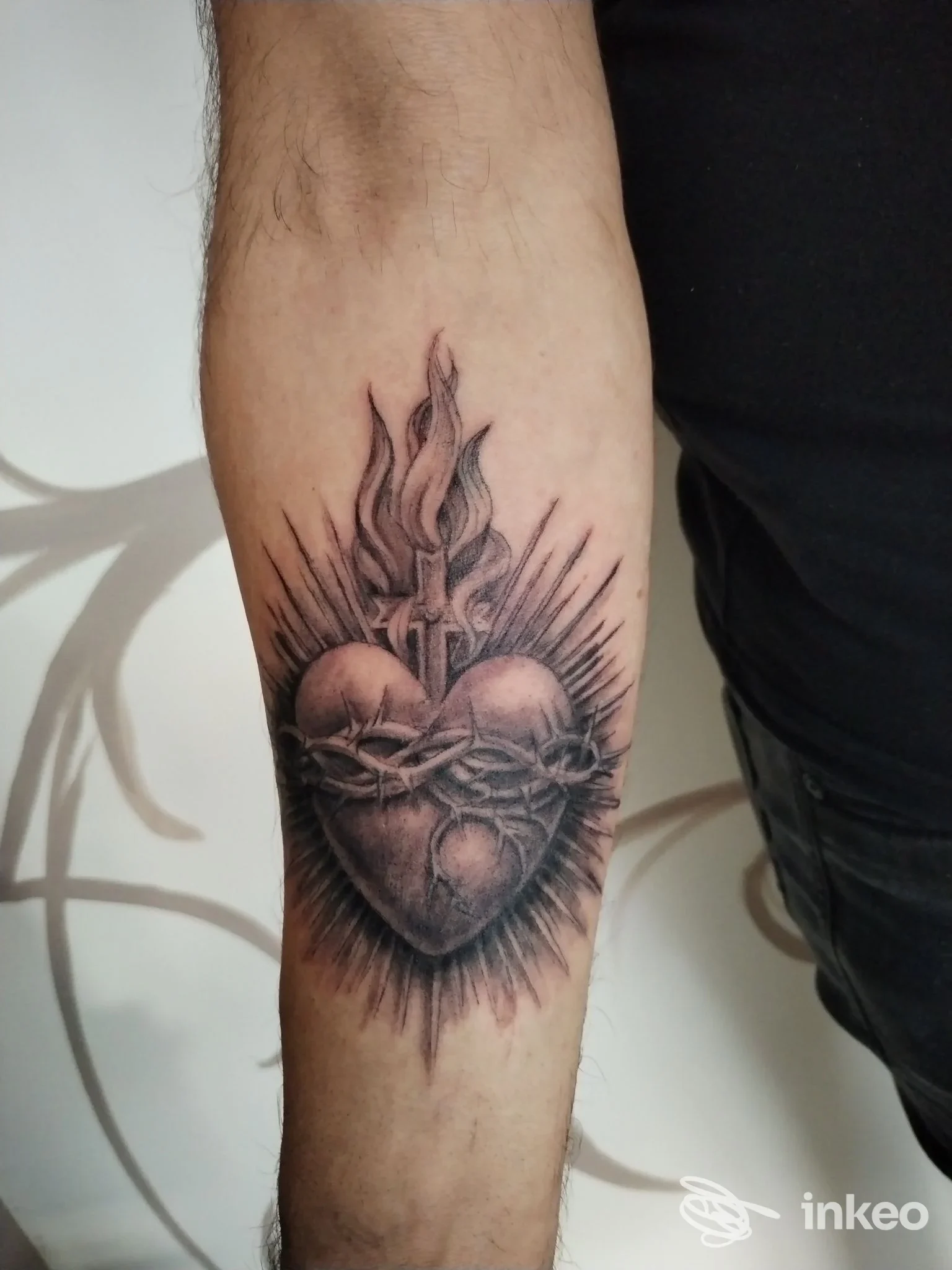 Tatuaggio realistico in bianco e nero su avambraccio: cuore trafitto da spina, raggi energetici e fiamme in alto; esecuzione dettagliata e ombreggiature marcate.