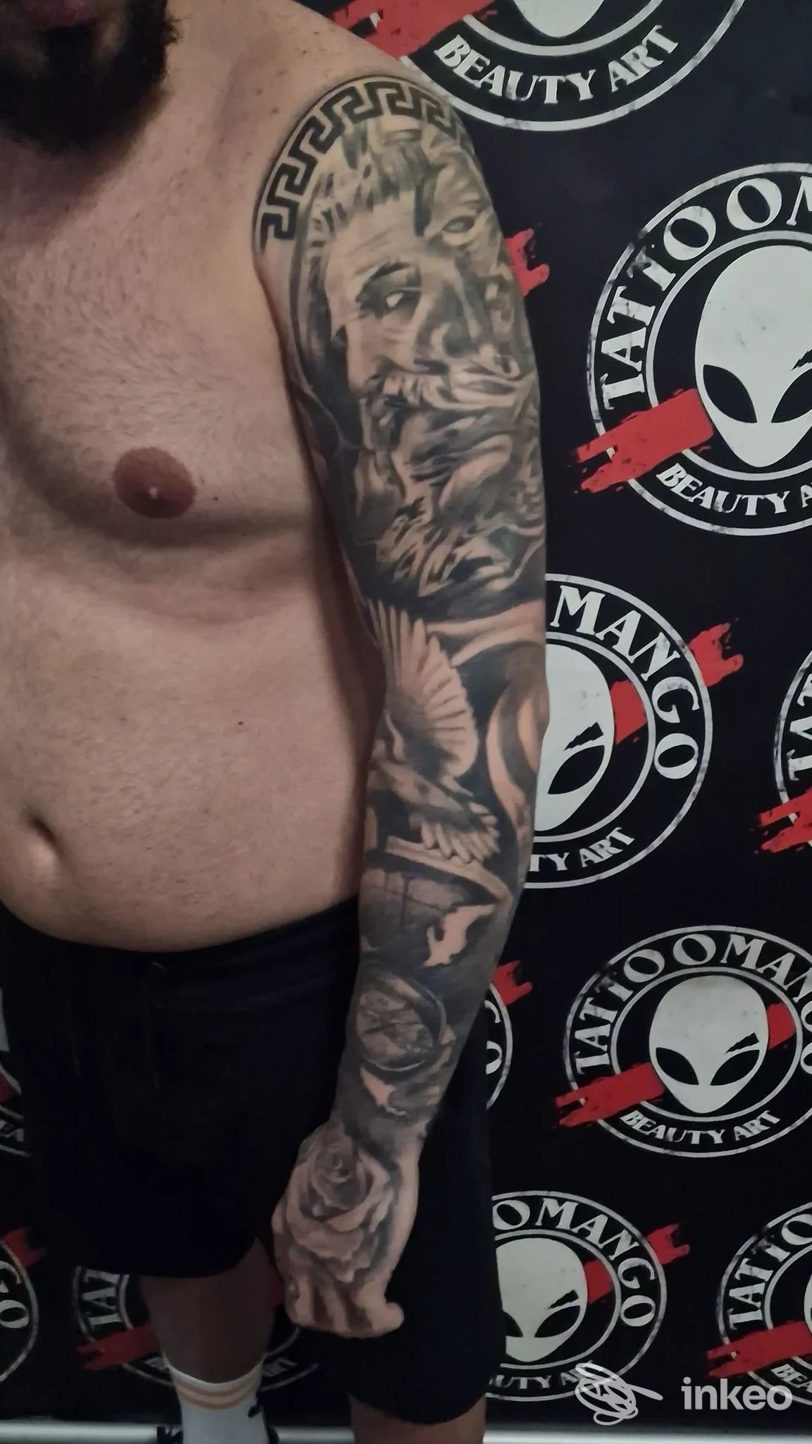 Braccio sinistro di un uomo con tatuaggio completo: ritratto femminile e motivi decorativi, sfondo con motivo di studio Tattoomango Napoli.