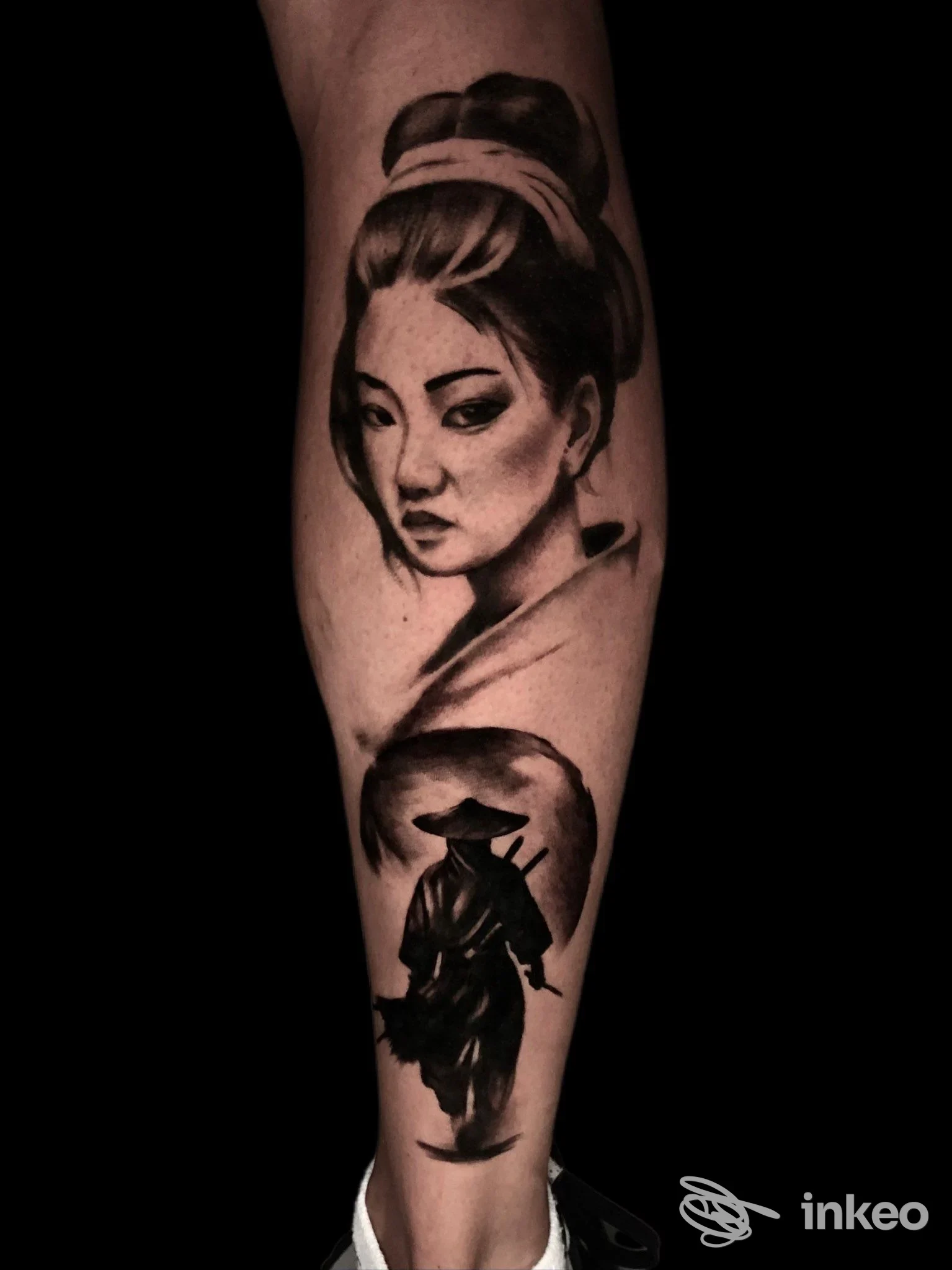Tatuaggio realistico su gamba: ritratto di geisha in nero/grigio, con un personaggio in silhouette sotto, sfondo scuro.