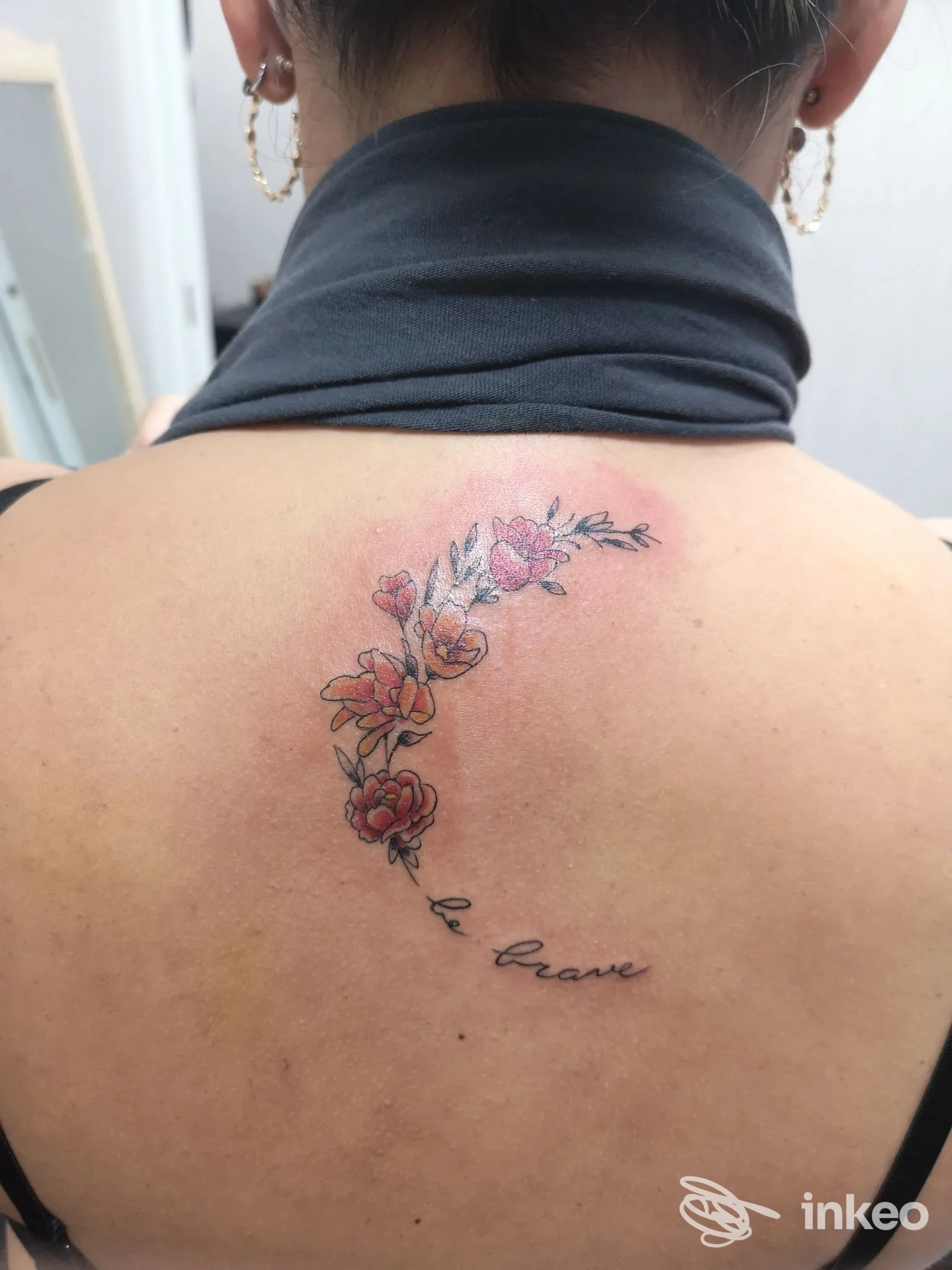 Tattoo floreale lungo la schiena, con fiori colorati e una scritta in corsivo sulla pelle, visibile tra le scapole dell’emergente. Uno scatto di studio senza watermark o testo promozionale.