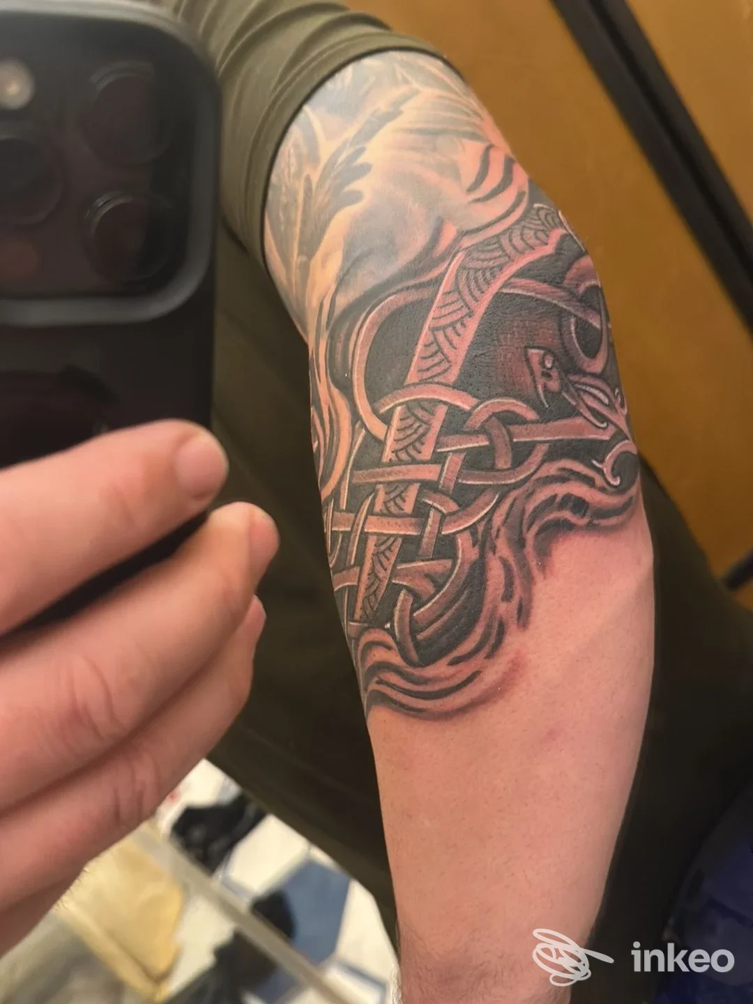 Braccio di una persona con tatuaggio in stile intrecciato/celtico visibile sul tessuto della pelle, tonalità nere e grigie, zoom che mette in mostra linee fitte e contorni detagliati.