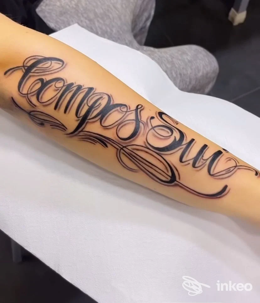 Tattoo script sull'avambraccio, linee fluide e ornamenti decorativi in nero, visibile su pelle umana, in uno studio di Napoli.