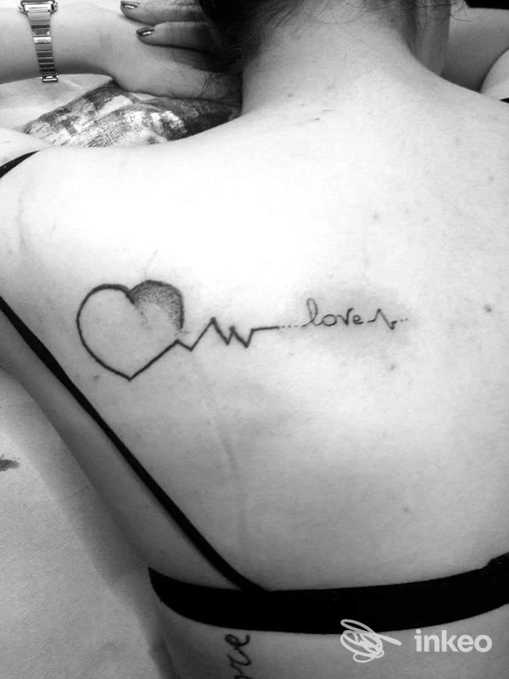 Tattoo reale sulla schiena: cuore con linea di ritmo e parola love, realizzata sulla pelle della persona, foto in bianco e nero.