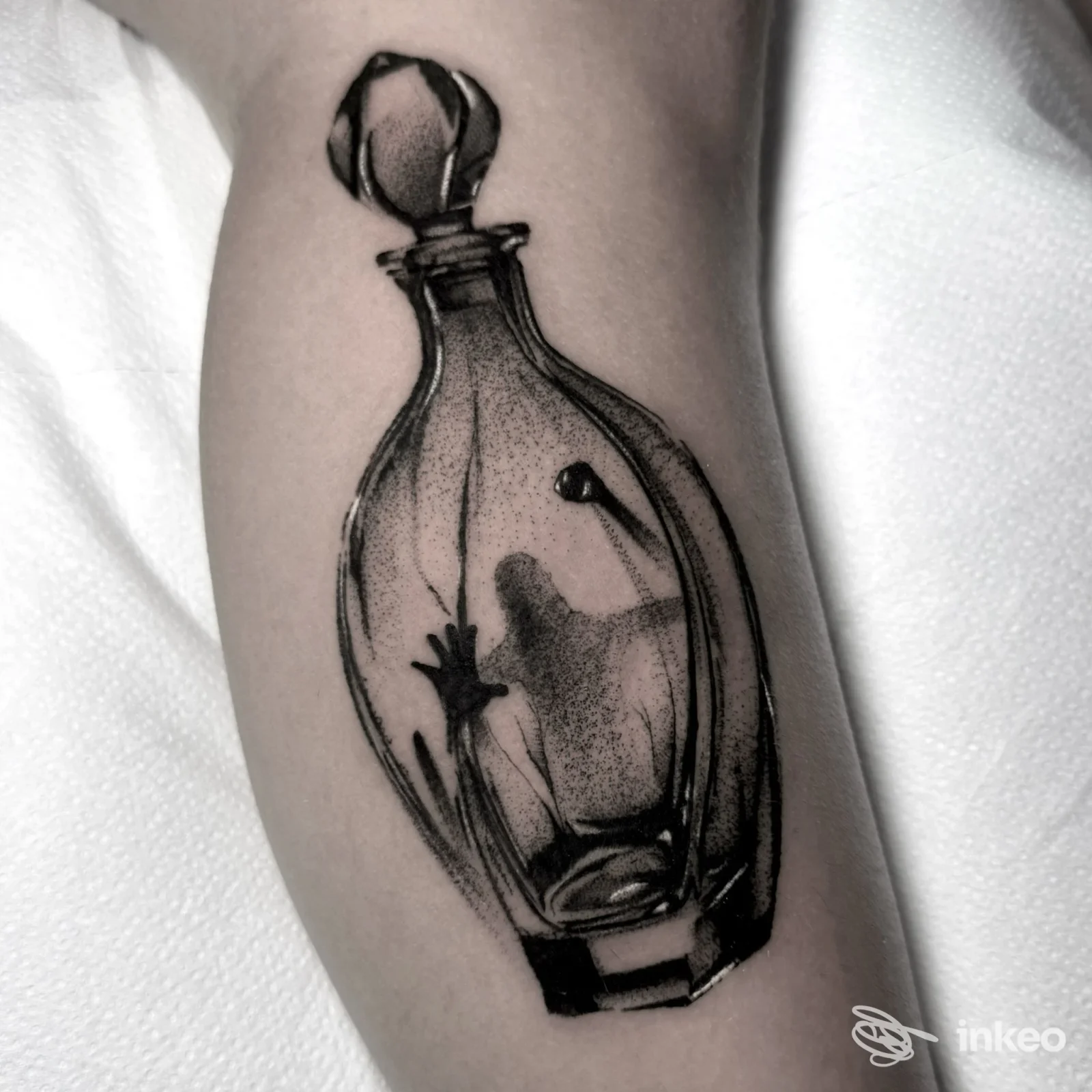Tattoo realistico su avambraccio raffigurante una bottiglia di vetro con riflessi e un fiore all'interno, in bianco e nero su pelle chiara, eseguito nello studio Black Tears Tattoo Studio di Pozzuoli.