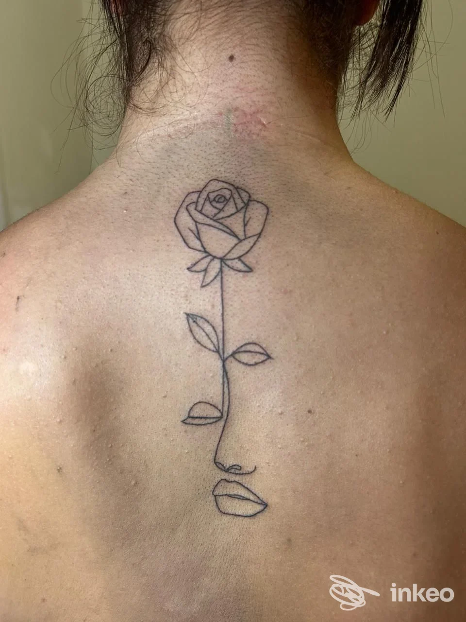 Tatuaggio lineare a motivo di rosa lungo la colonna vertebrale, visibile sulla schiena dal collo alle spalle, realizzato direttamente sulla pelle.