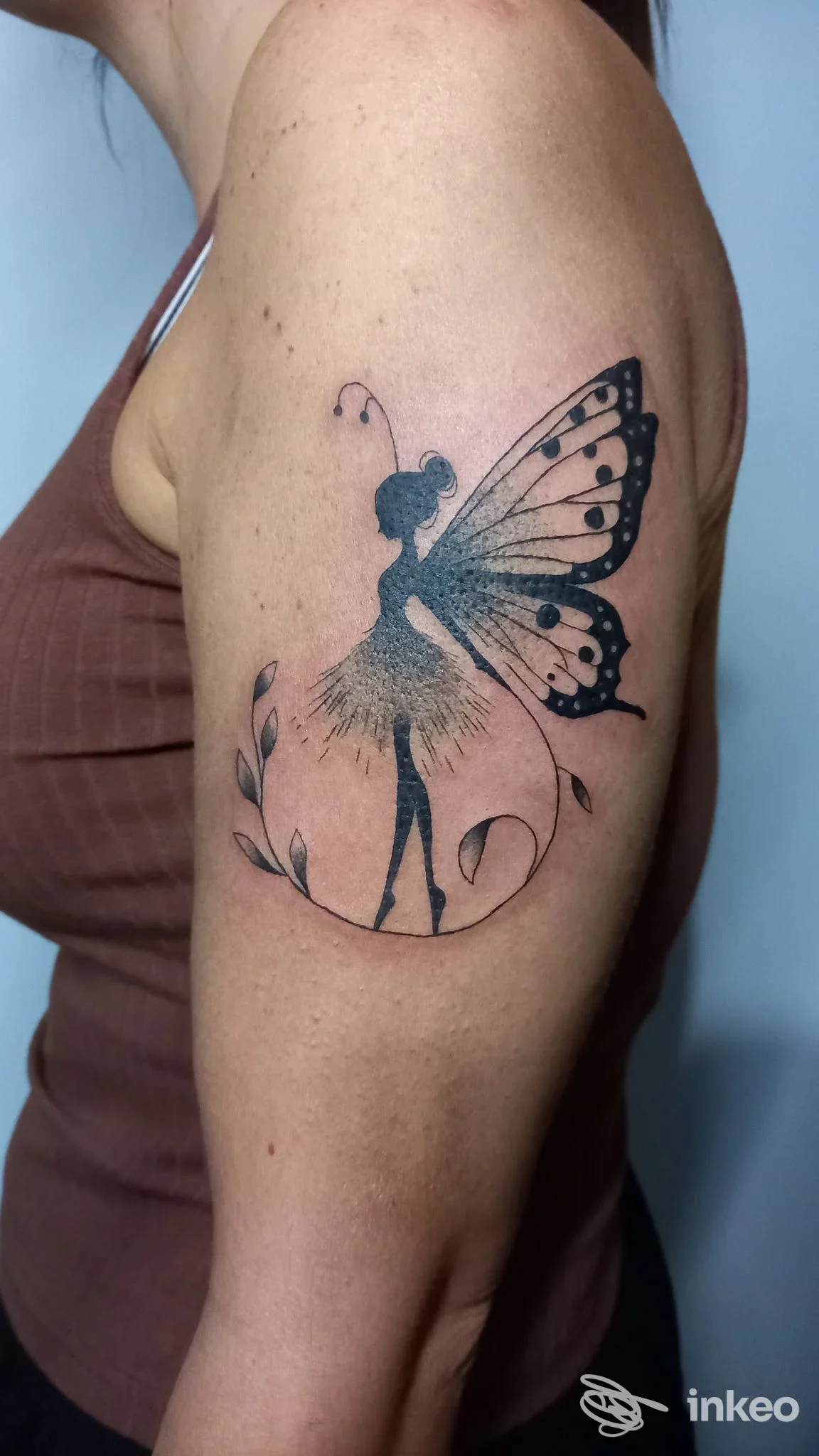 Tattoo sul braccio raffigurante una fata farfalla con ali stilizzate e fioriture, eseguito su pelle, in studio.