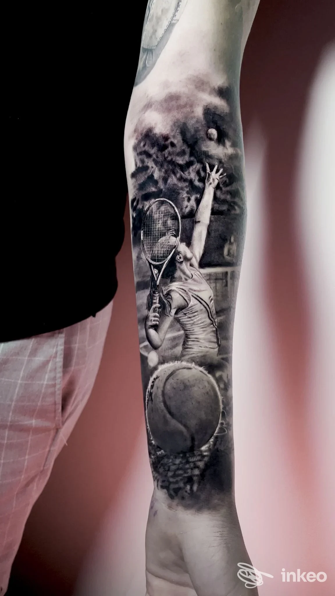 Avambraccio sinistro con tatuaggio realistico in bianco e nero raffigurante una scena di tennis; l'immagine mostra solo la porzione di pelle tatuata.