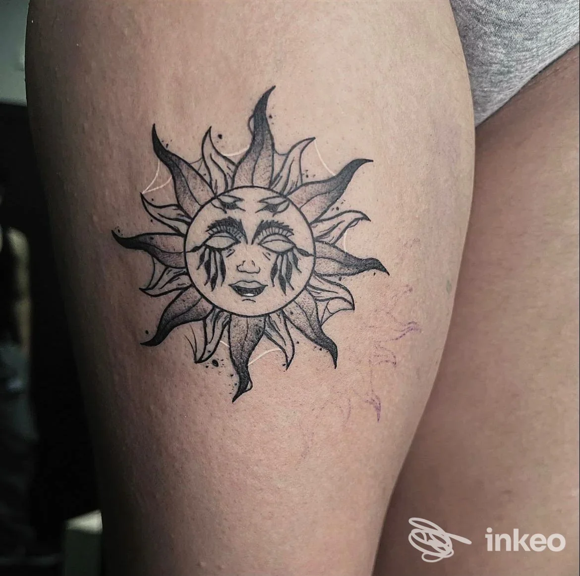Tattoo a forma di sole stilizzato con volto sorridente, posizionato sulla parte superiore del braccio, in tinta nera su pelle chiara, realizzato da studio non specificato.