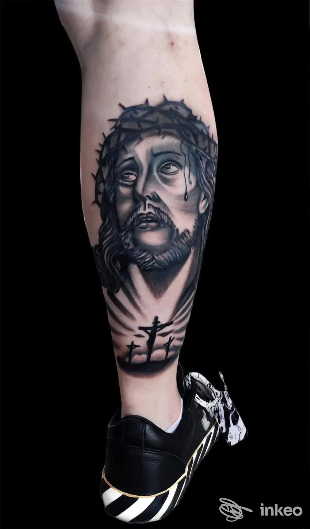 Tattoo sul polpaccio raffigurante Gesù con corona di spine, realizzato da Stigma Tattoo Studio, Acerra, in bianco e nero, parte inferiore della gamba e abbigliamento sportivo visibile.