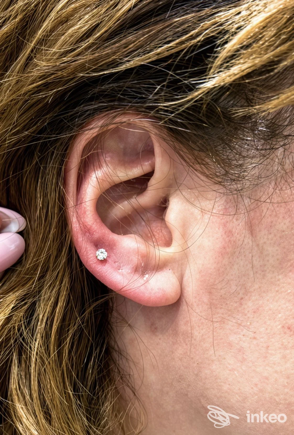 Orecchio di una persona con un piccolo piercing al lobo, brillante zircone, visibile in primo piano; studio Love & Hate Tattoo & Piercing Studio a San Nicola la Strada.