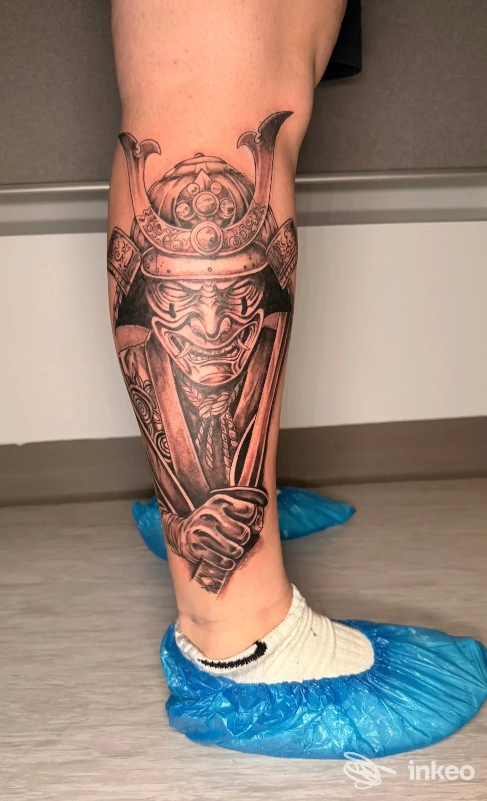 Tattoo sul polpaccio raffigurante un guerriero samurai con elmo, realizzato in bianco e nero sulla pelle, visibile senza volto completamente.