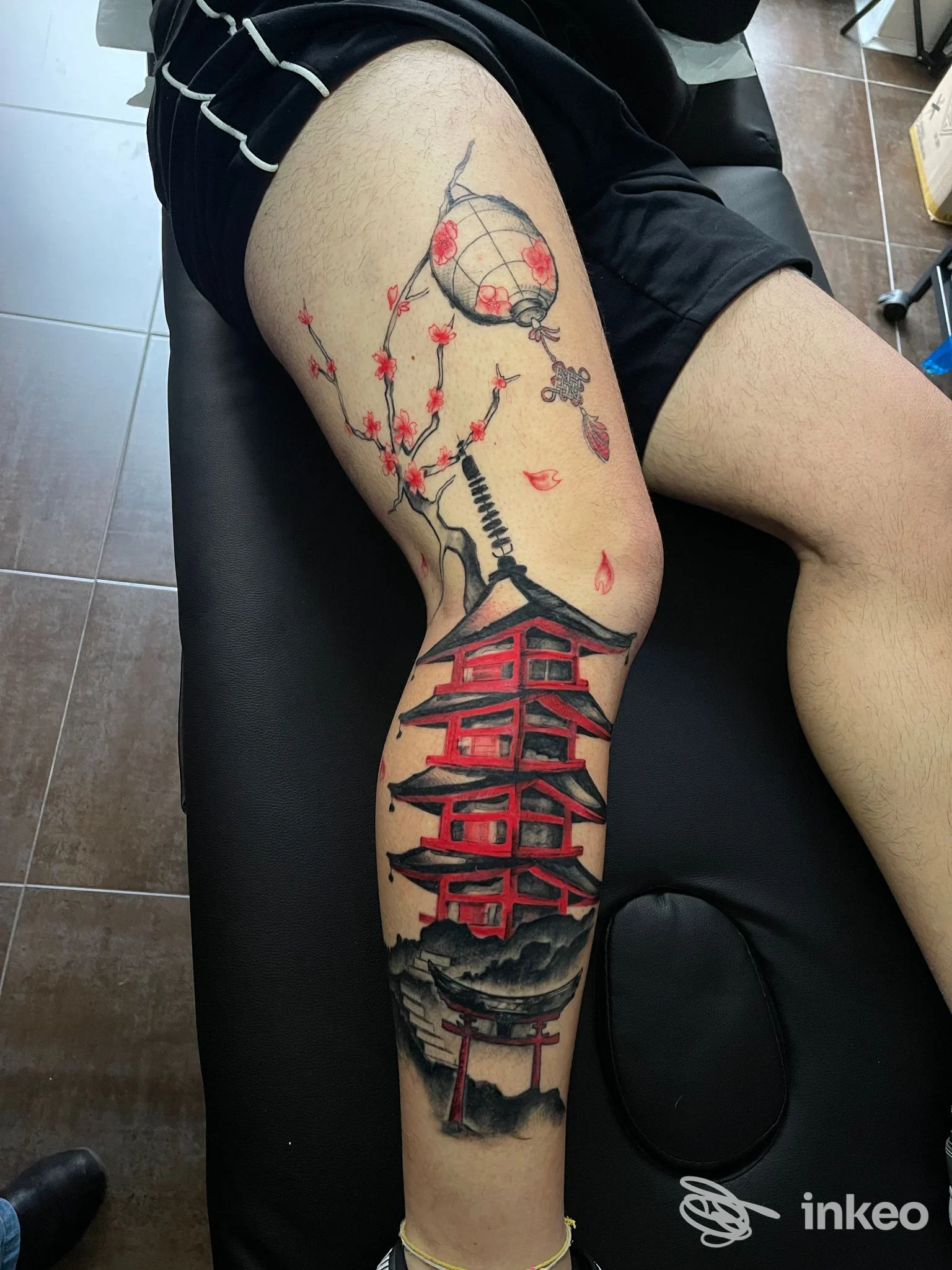 Tattoo colorato su polpaccio raffigurante una pagoda rossa, alberi fioriti e lanterna, eseguito su pelle reale.