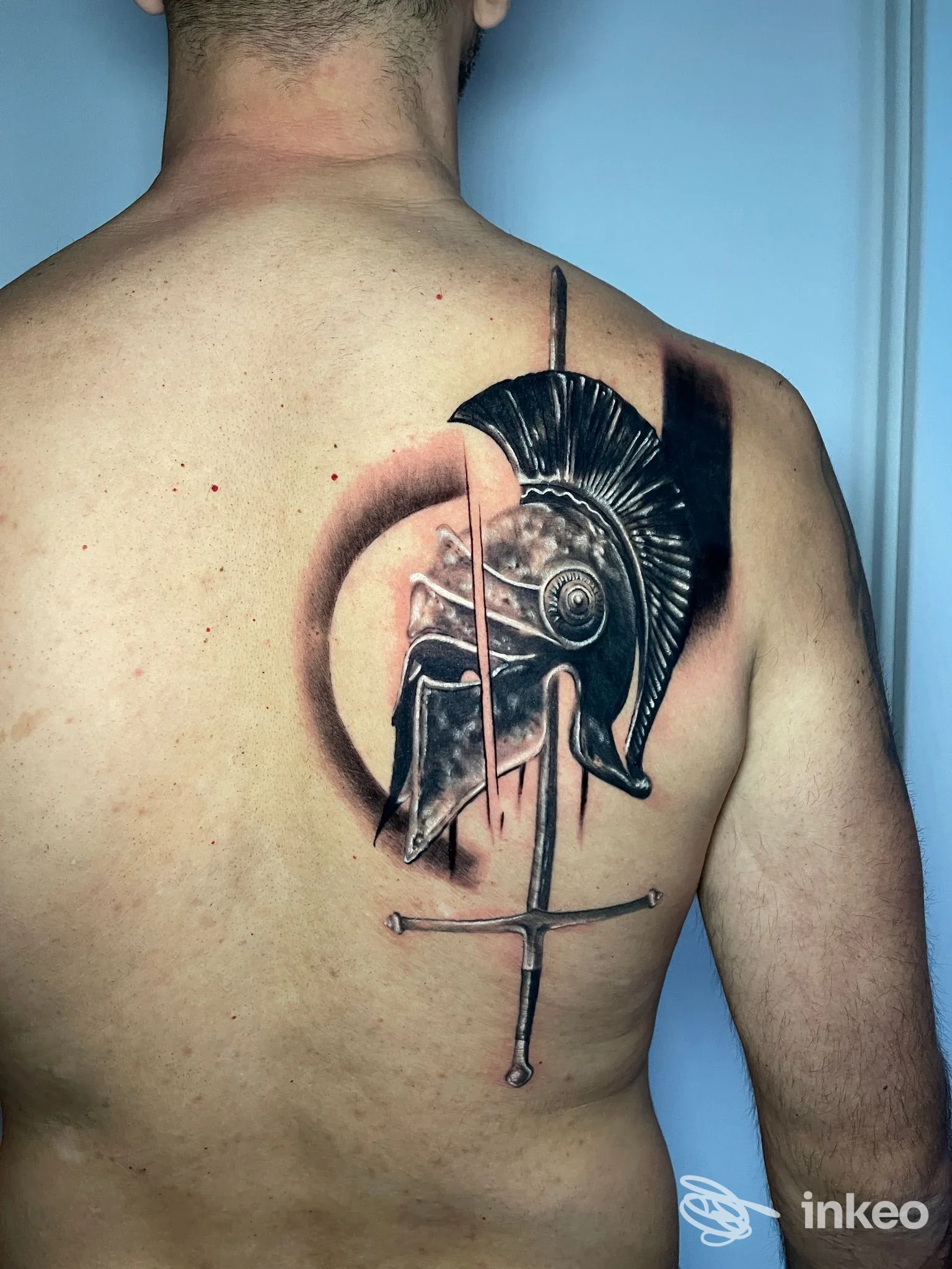 Tattoo grande sulla schiena di un uomo: elmo romano, arco e freccia, eseguito da Drop Ink Tattoo E Piercing a Napoli, visibile dall’indietro.