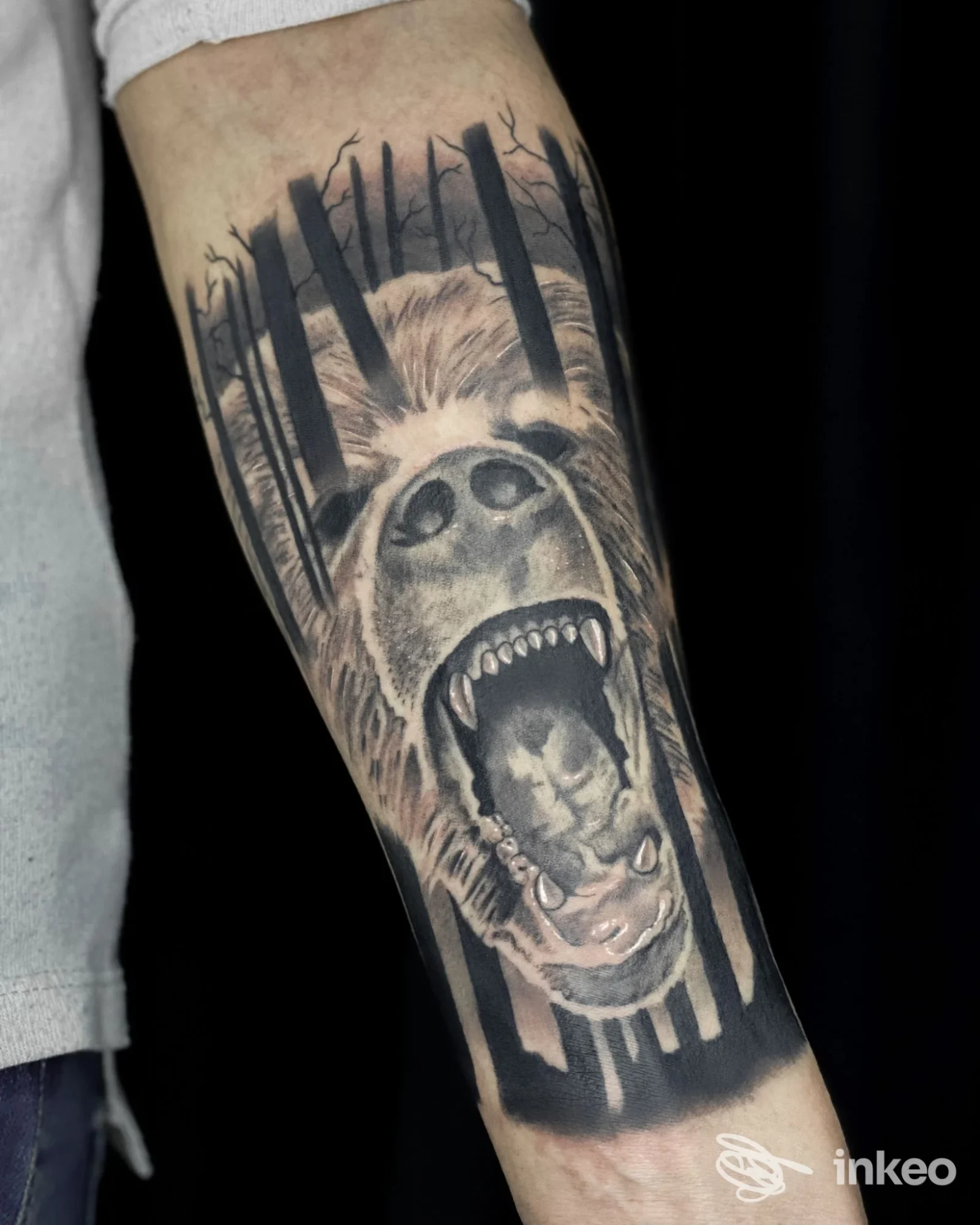 Tatuaggio realistico su avambraccio raffigurante una creatura urlante in stile dark, con fauci aperte e foresta sullo sfondo, eseguito sulla pelle del soggetto.